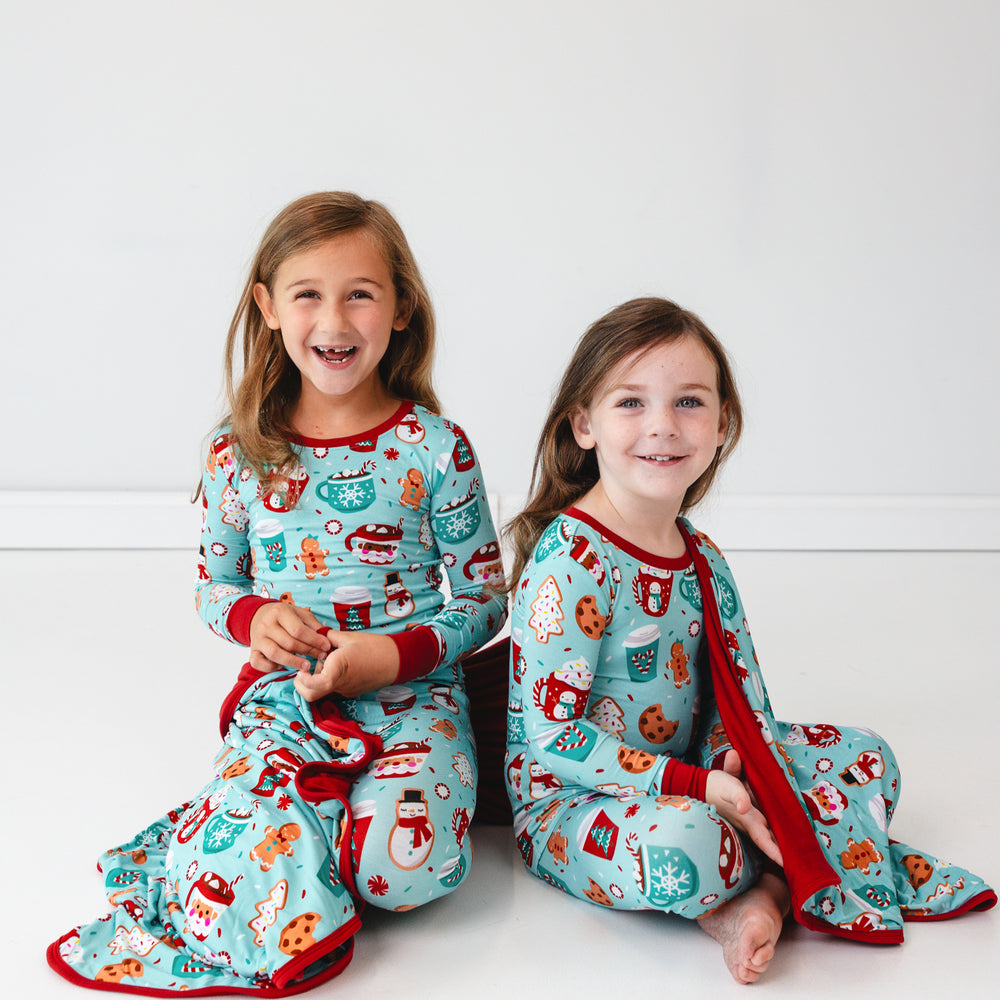 Two children sitting on the ground with a Peppermint Mocha Large Cloud Blanket around them and wearing matching pajamas.