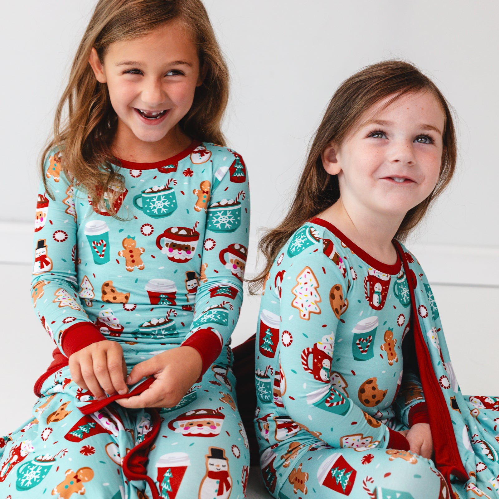 Close up image of two children sitting on the ground wearing Peppermint Mocha Two-Piece Pajama Sets