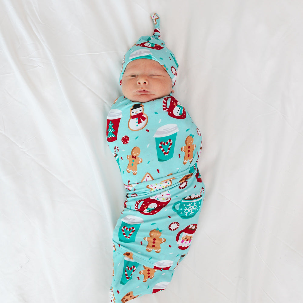 Image of an infant laying on a blanket swaddled in a Peppermint Mocha Swaddle and Hat Set