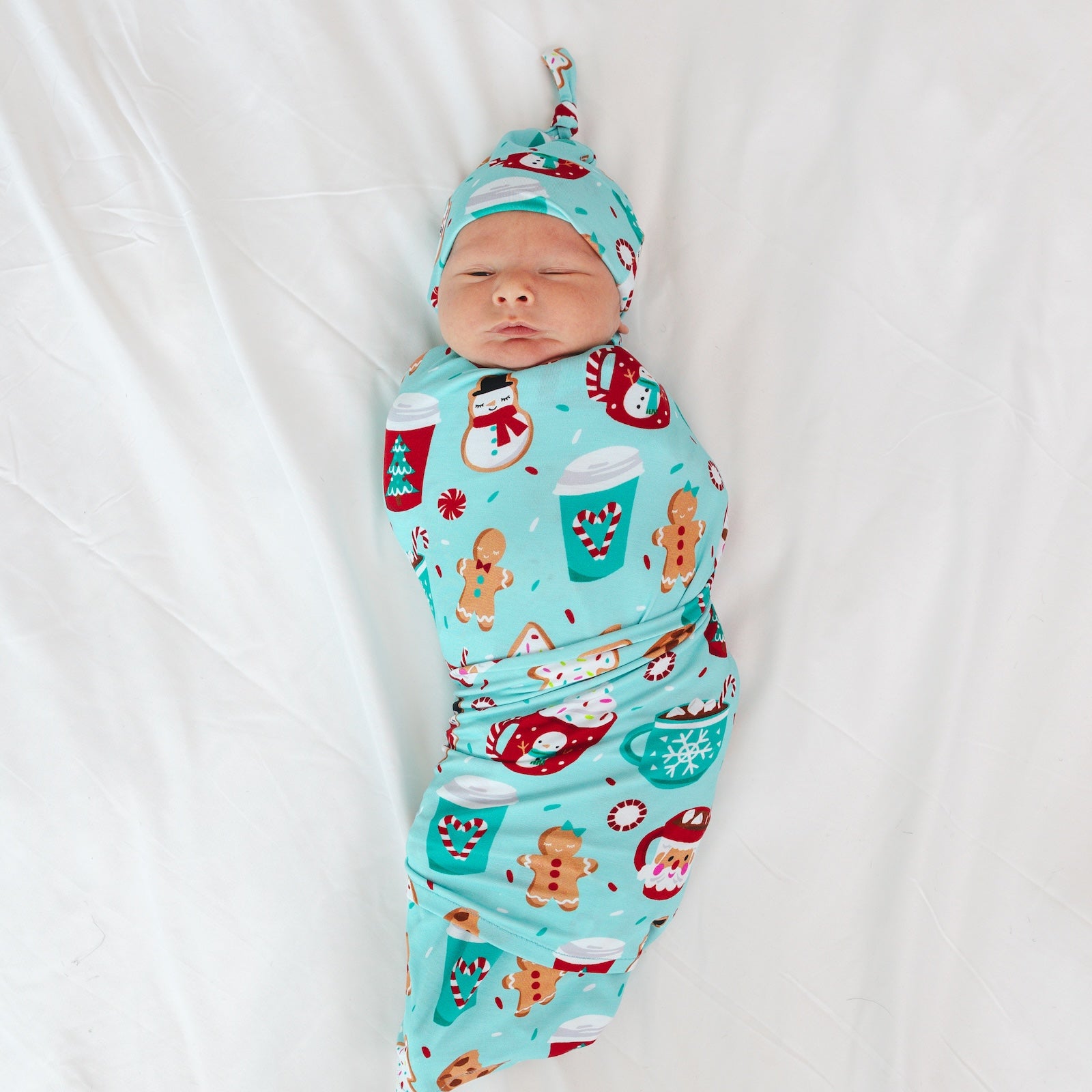 Image of an infant laying on a blanket swaddled in a Peppermint Mocha Swaddle and Hat Set