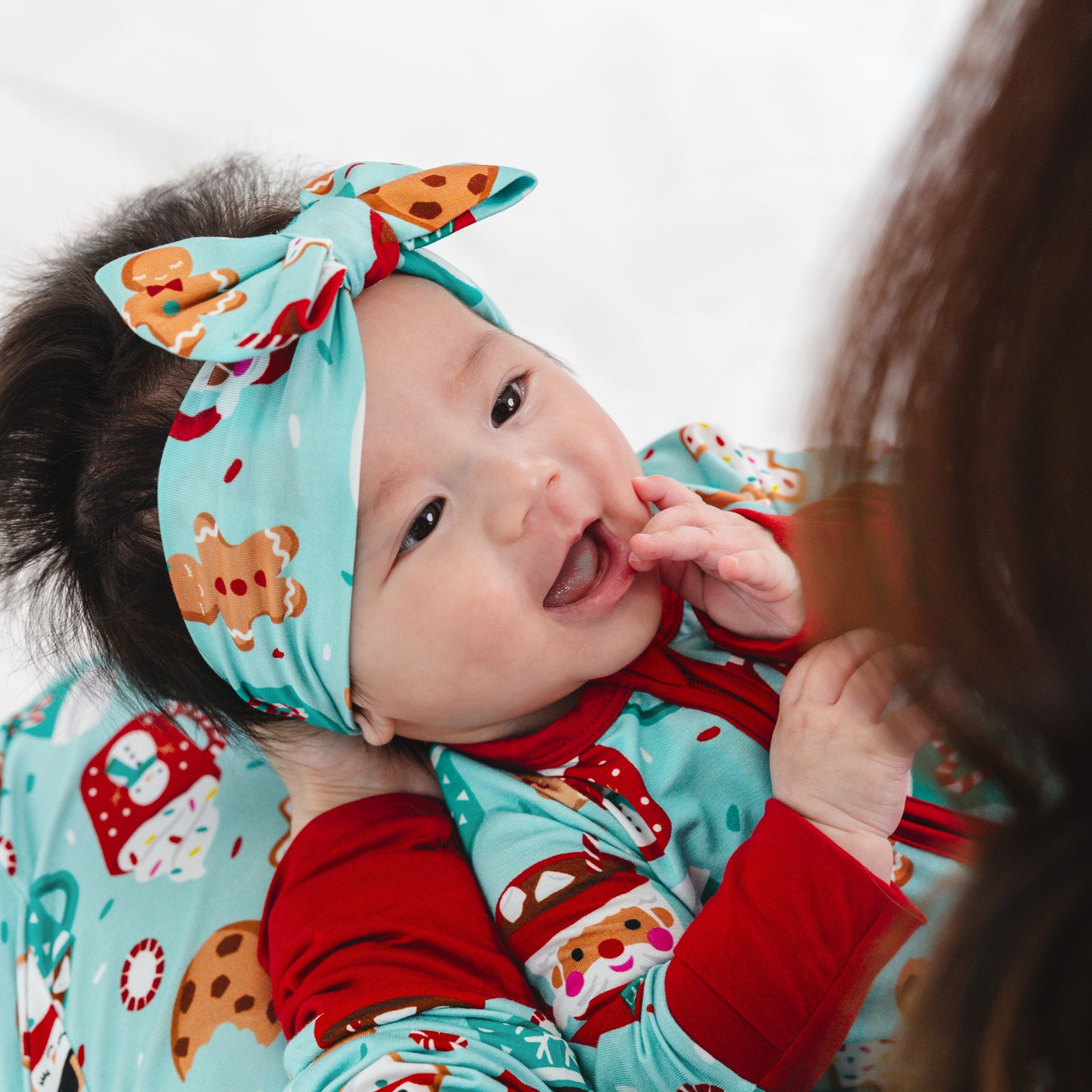 Close up image of a child being held by a parent wearing a Peppermint Mocha Luxe Bow Headband and matching Zippy.