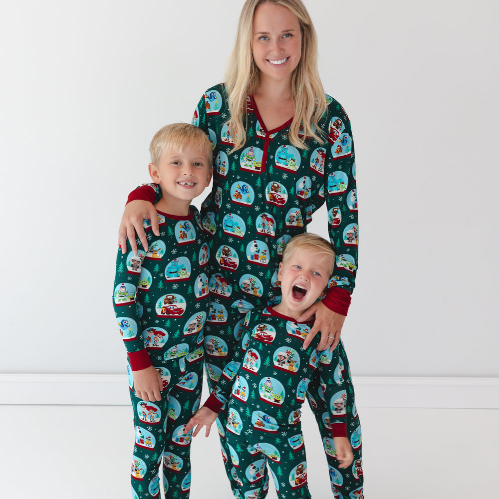 Boys are in the Disney A Very Pixar Christmas Two-piece Pajama Set. Smiling mother is in the middle of them while wearing the Disney A Very Pixar Christmas Women's Pajama Pants and Top