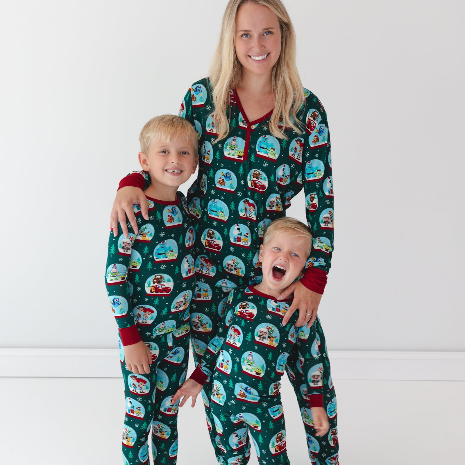 Boys are posing while wearing the Disney A Very Pixar Christmas Two-Piece Pajama Set, mother in the middle is wearing the Disney A Very Pixar Christmas Women's Pajama Top and Pants