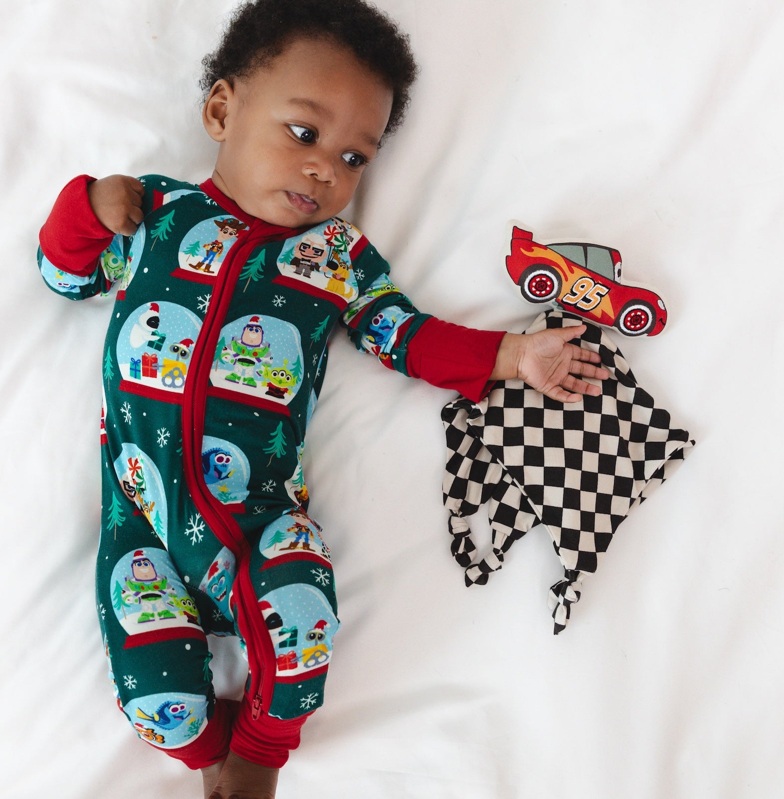 Top view image of baby laying down wearing the Disney A Very Pixar Christmas Zippy while next to the Disney Cars Lightning McQueen Lovey