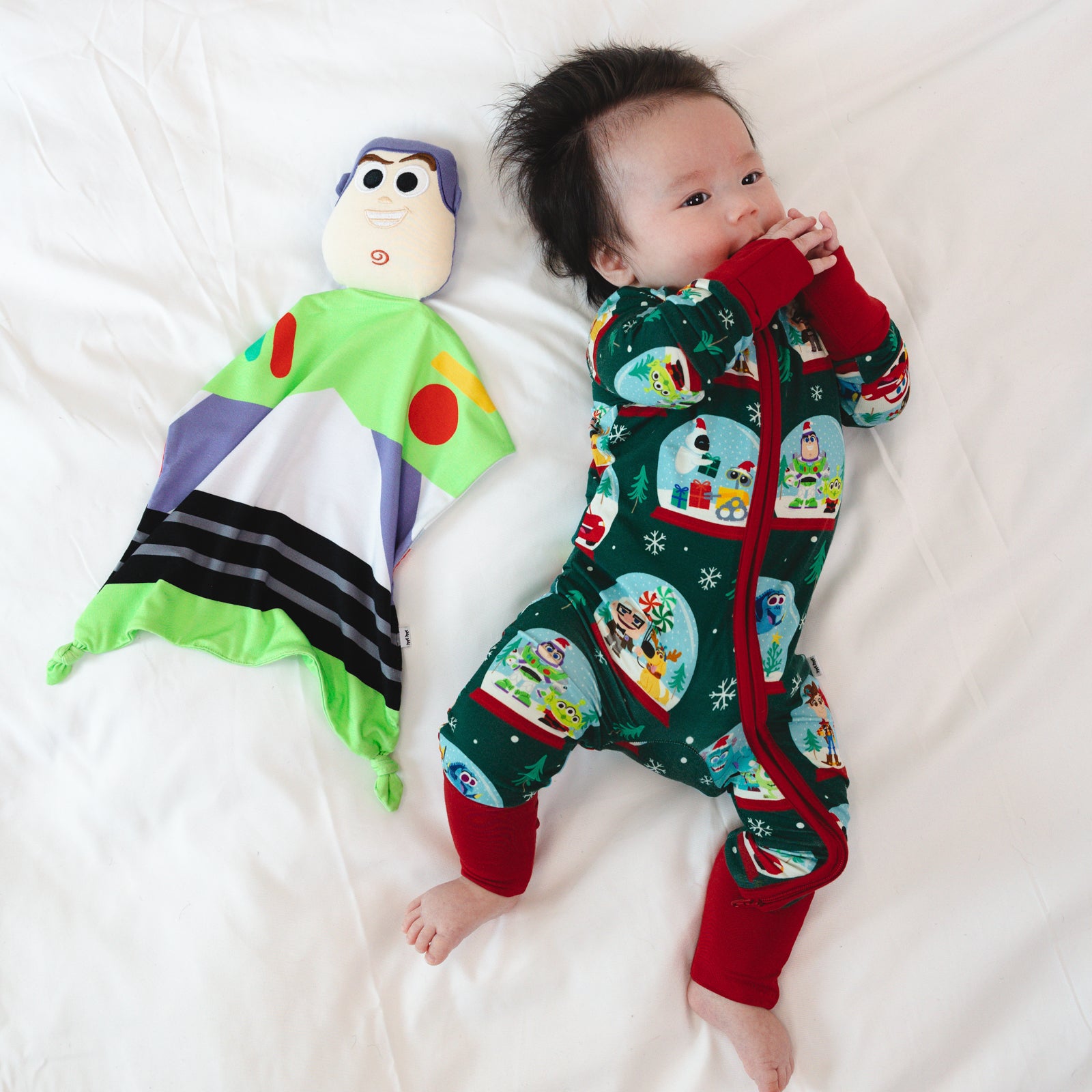 Top view image of baby laying down while wearing the Disney A Very Pixar Christmas Zippy, next to the Disney Toy Story Buzz Lightyear Lovey