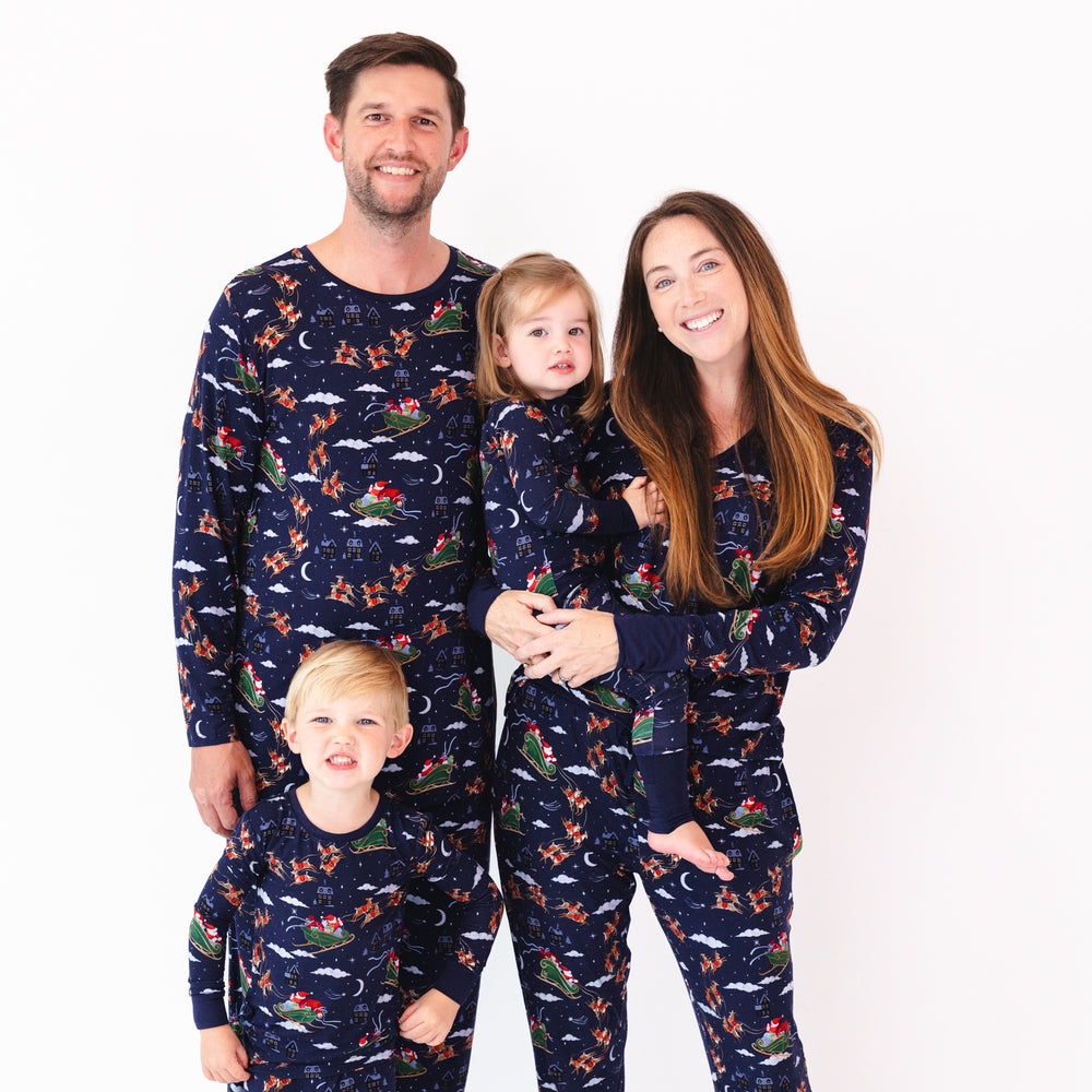 full family wearing Santa's Sleigh printed matching pajamas with mom holding a baby wearing a zippy.