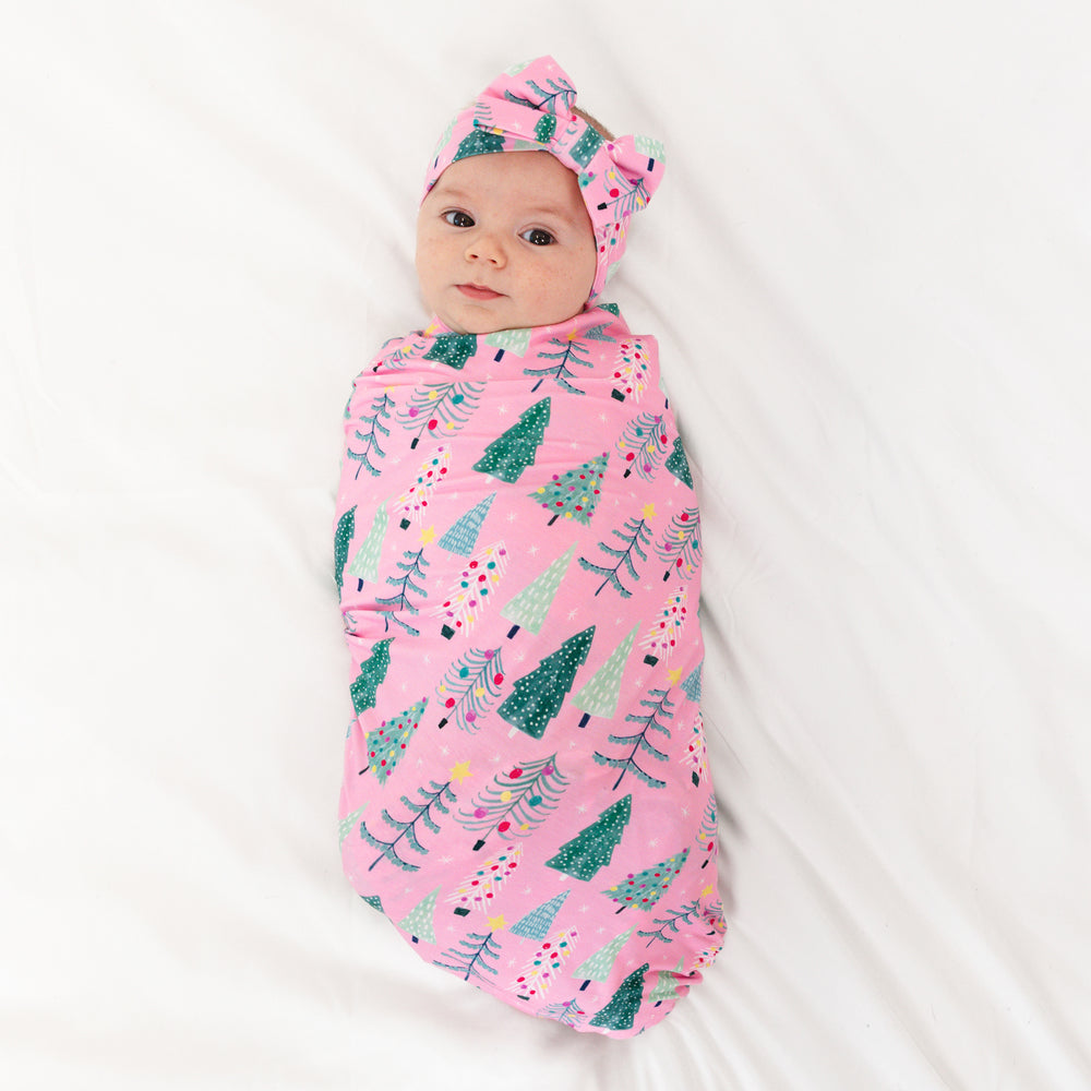 Image of an infant laying on a blanket swaddled in a Pink Twinkling Trees Swaddle and Luxe Bow Headband Set