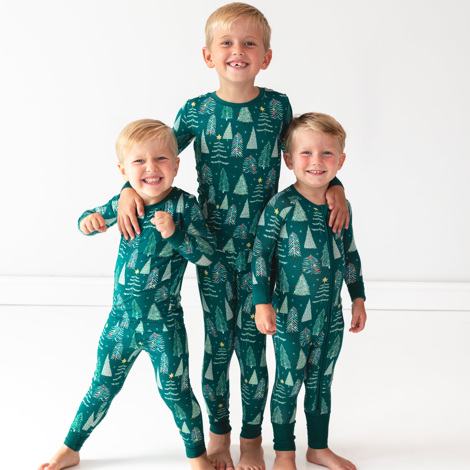 Three smiling boys wearing the Green Twinkling Trees Two-Piece Pajama Set together