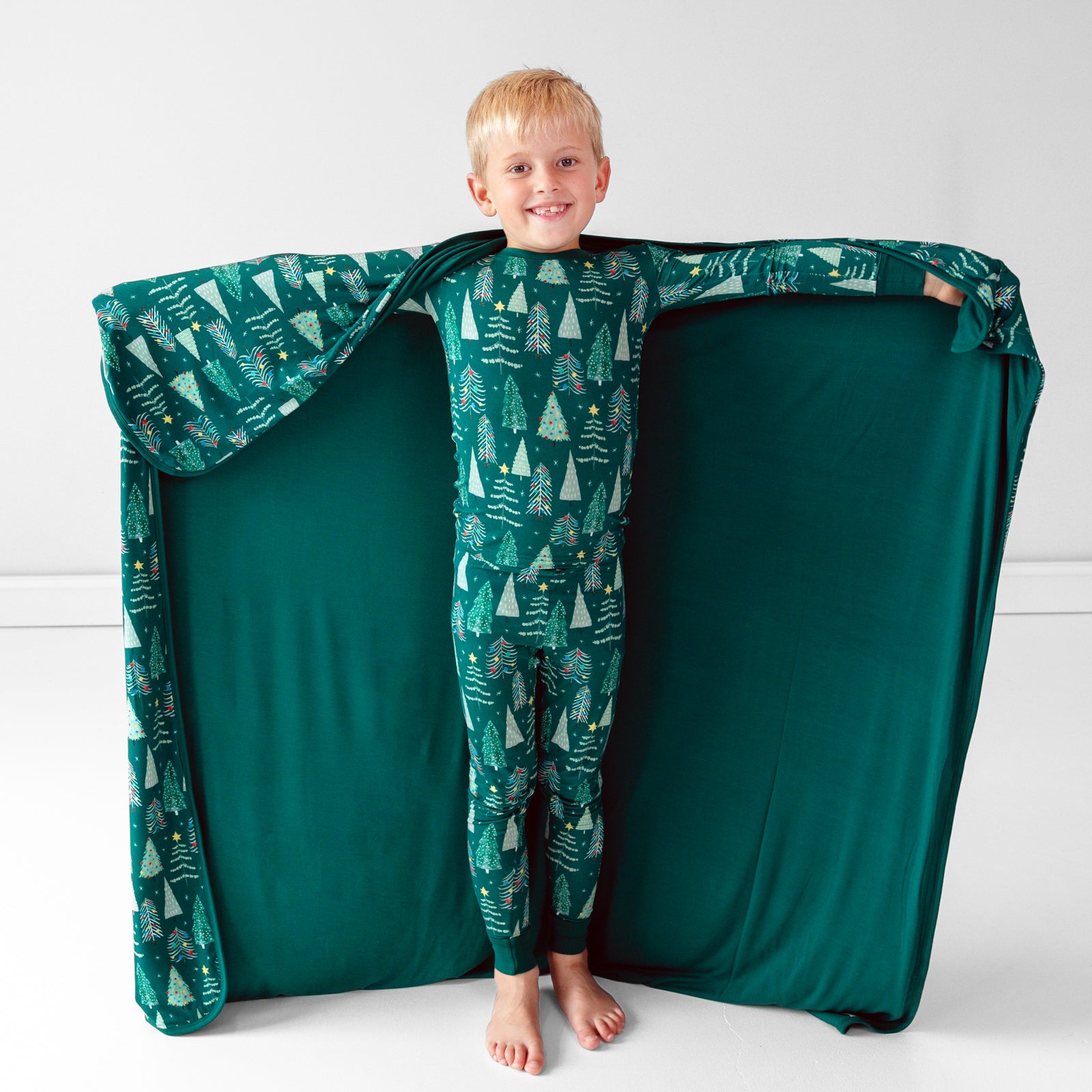 Smiling child posing with the Green Twinkling Trees Large Cloud Blanket® while displaying the inside green color