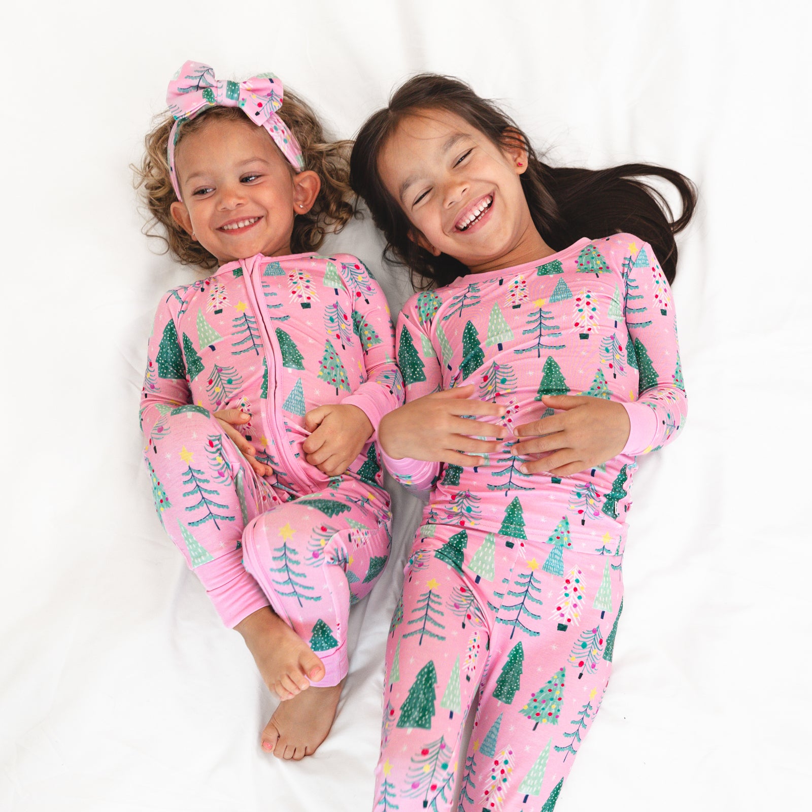 Two children laying on a blanket wearing matching Pink Twinkling Trees pajamas