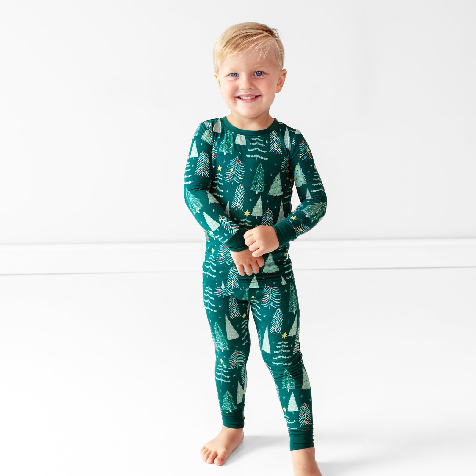 Smiling boy wearing the Green Twinkling Trees Two-Piece Pajama Set