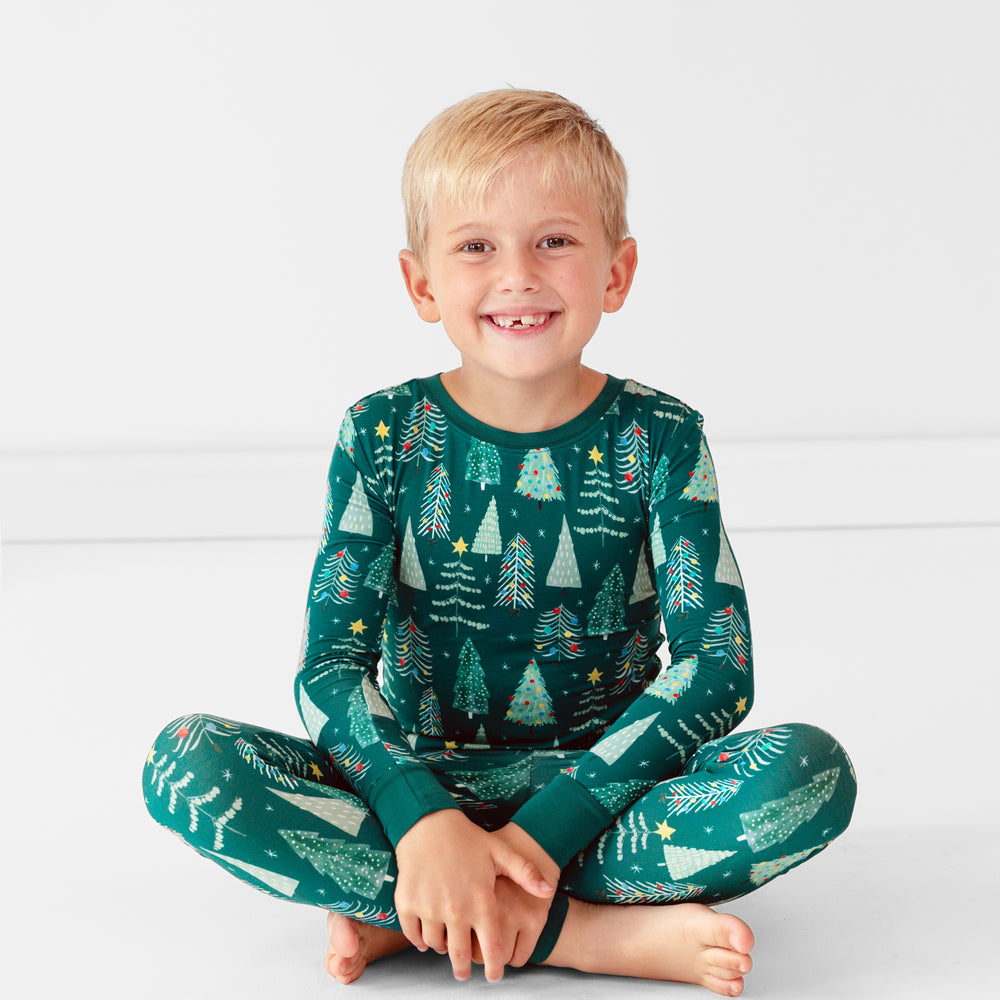 Smiling boy sitting while wearing the Green Twinkling Trees Two-Piece Pajama Set