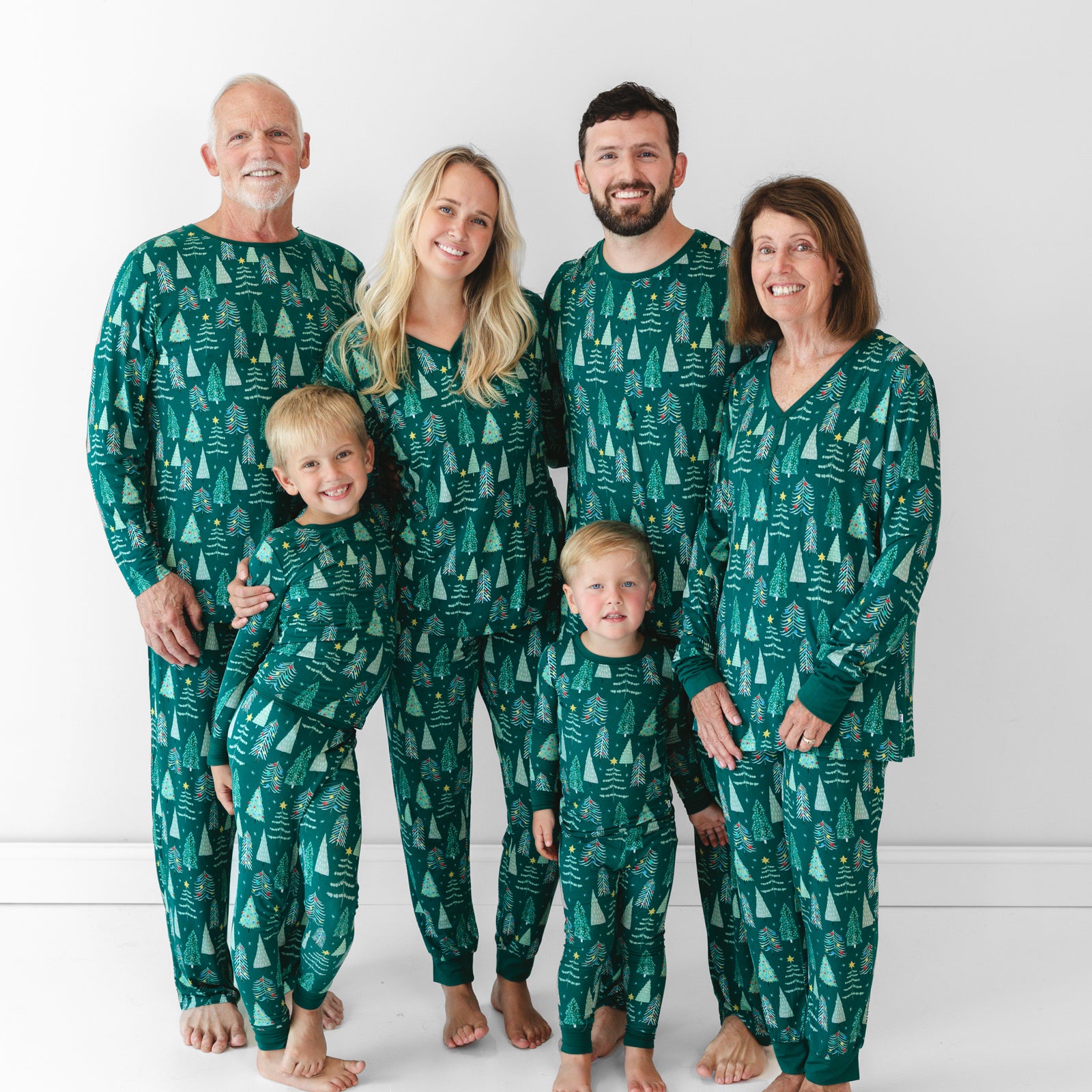 Image of a family of six wearing the Green Twinkling Trees print. Male model on the left is in the Green Twinkling Trees Men's Pajama Pants and Top. Both children are wearing the Green Twinkling Trees Two-piece Pajama Set. Female model in the middle is wearing Green Twinkling Trees Women's Pajama Pants and Top while male model on the right of her is in the Green Twinkling Trees Men's Pajama Pants and Top. Female model on the far right is also wearing the Green Twinkling Trees Women's Pajama Pants and Top