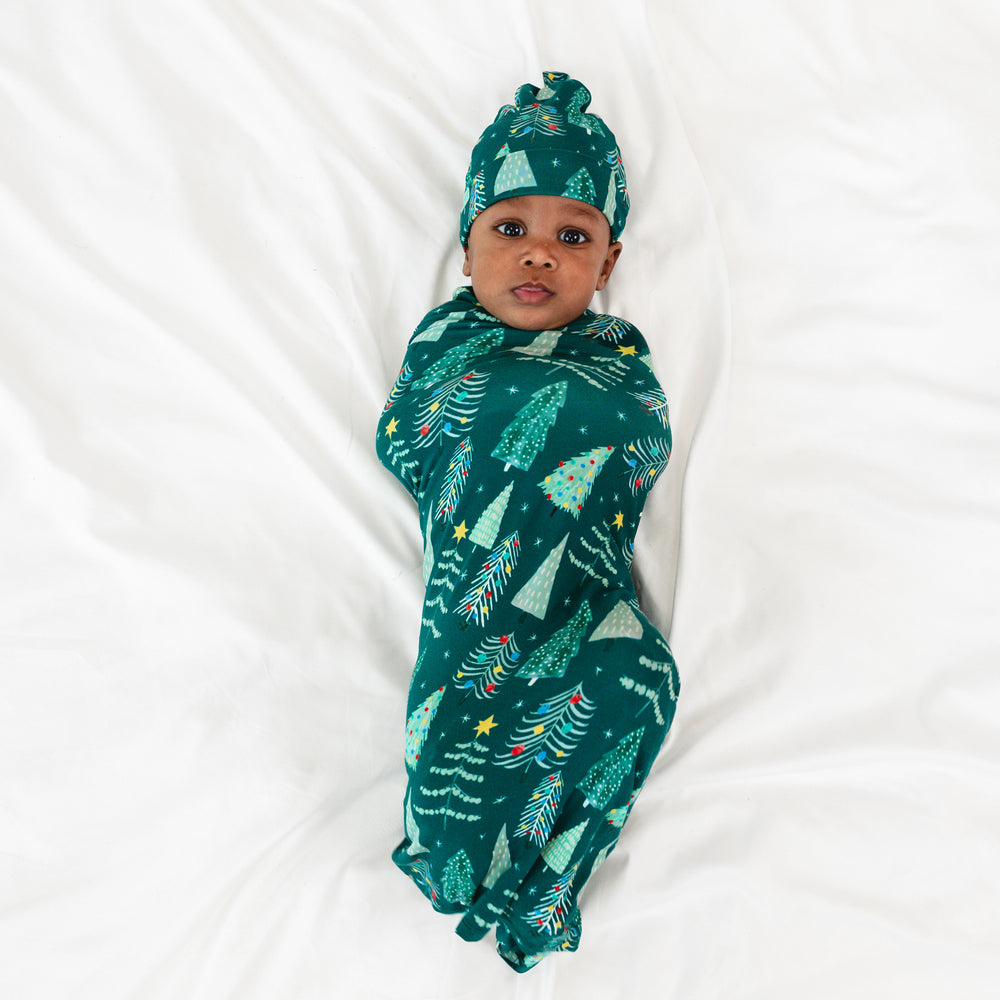 Top view image of baby laying down while in the Green Twinkling Trees Swaddle & Hat Set