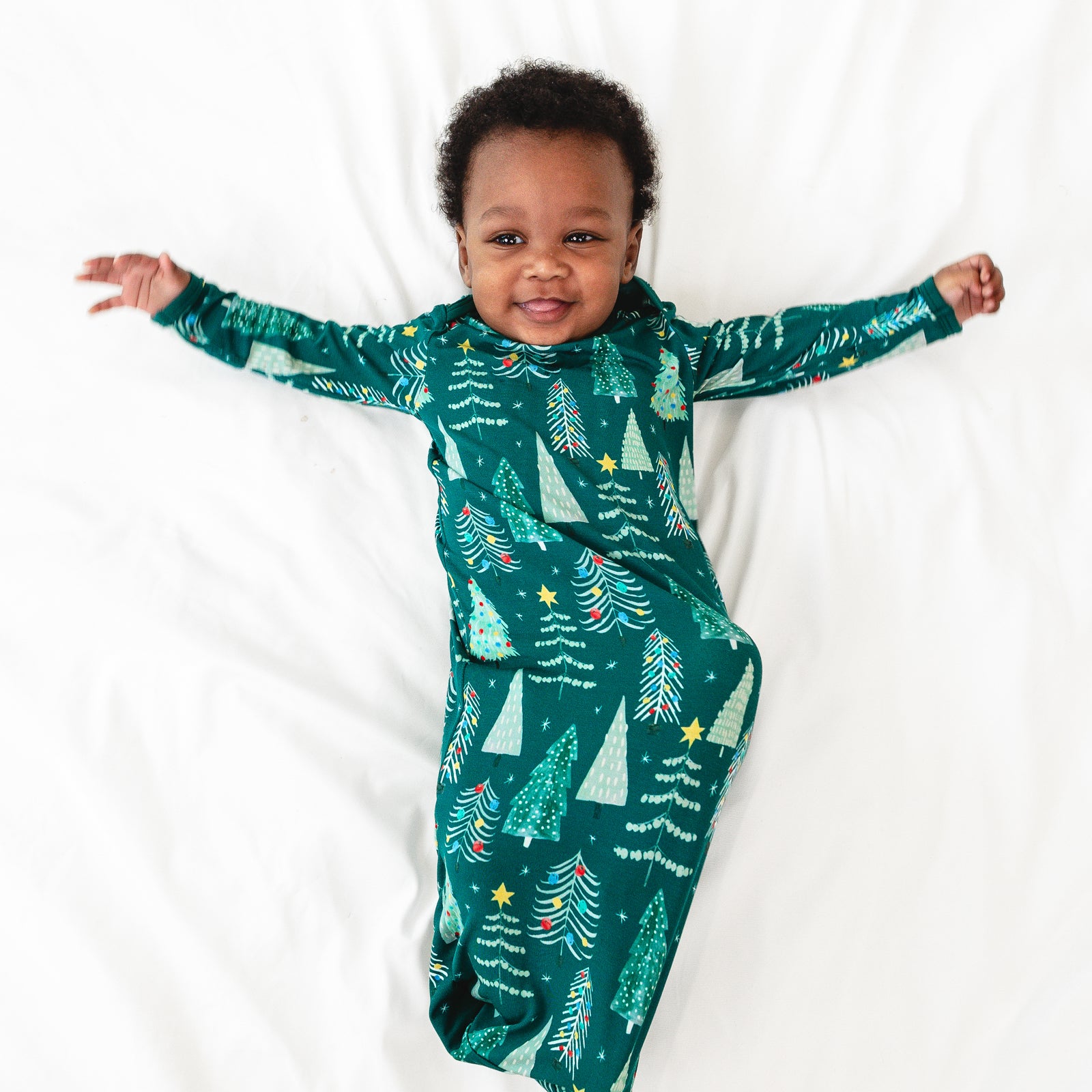 Alternative top view image of baby laying down with arms stretched out while wearing the Green Twinkling Trees Infant Gown