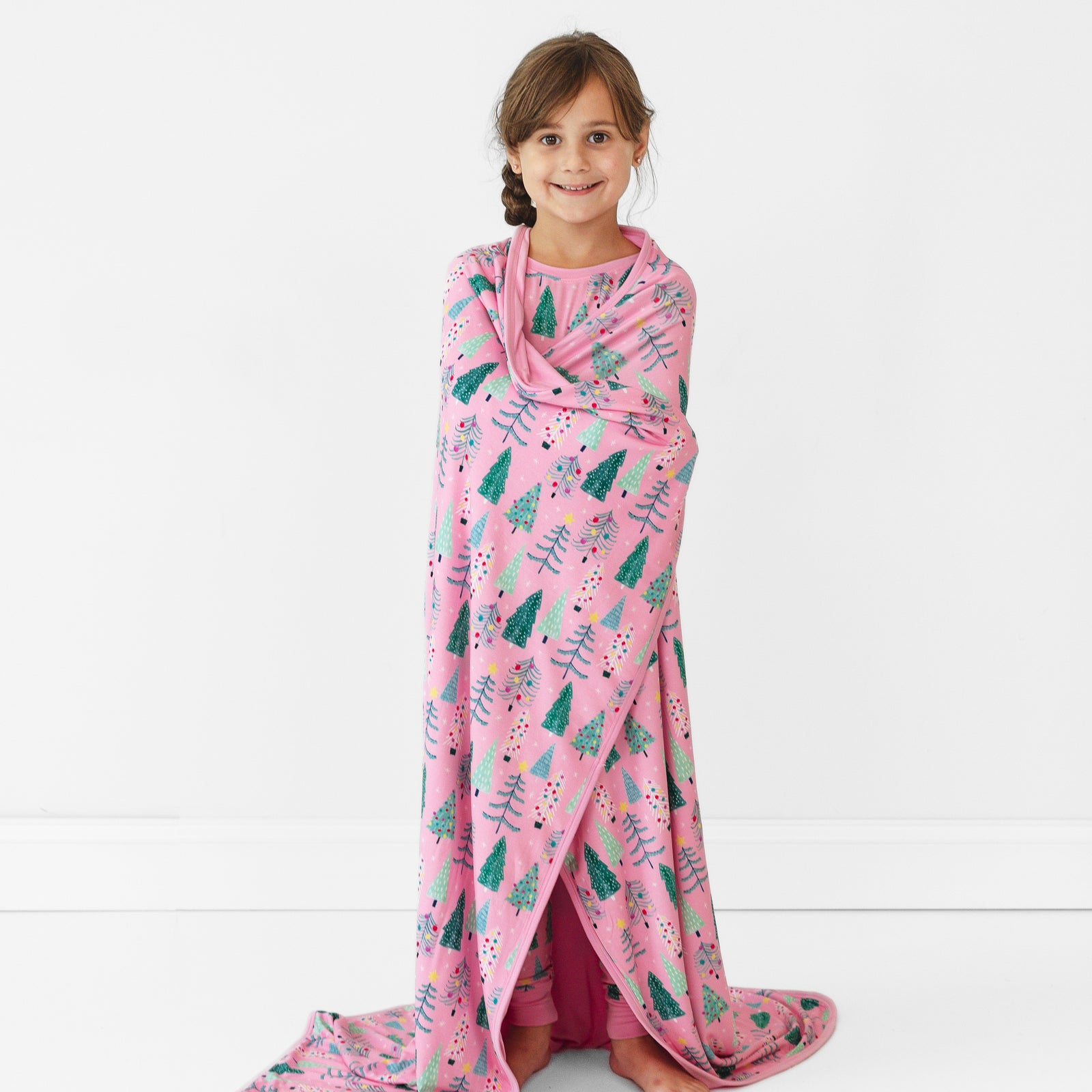 Child standing with a Pink Twinkling Trees Large Cloud Blanket wrapped around them and wearing matching pajamas