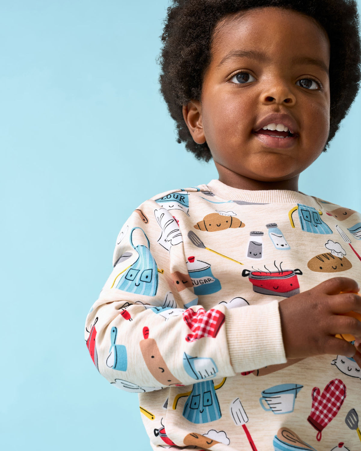 Close up of boy wearing the Little Chef Crewneck Sweatshirt on a blue background