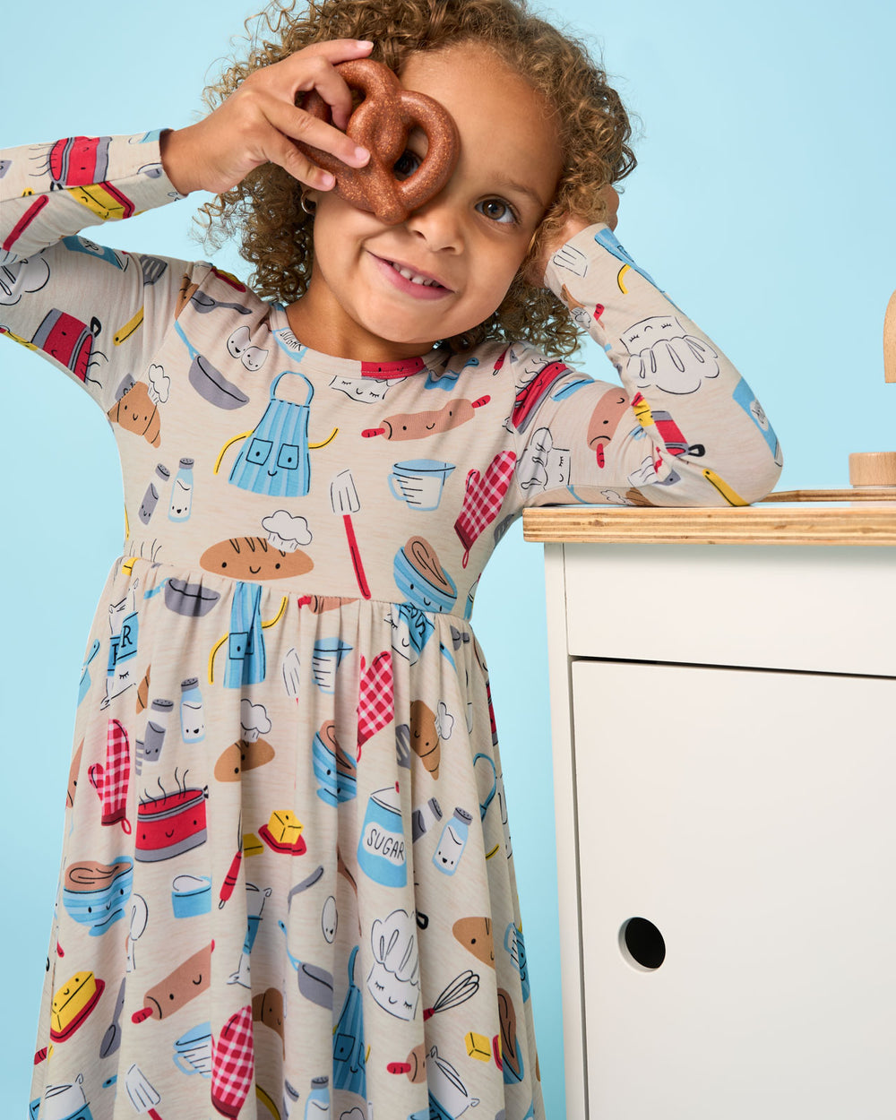 Girl wearing the Little Chef Twirl Dress hold a toy pretzel