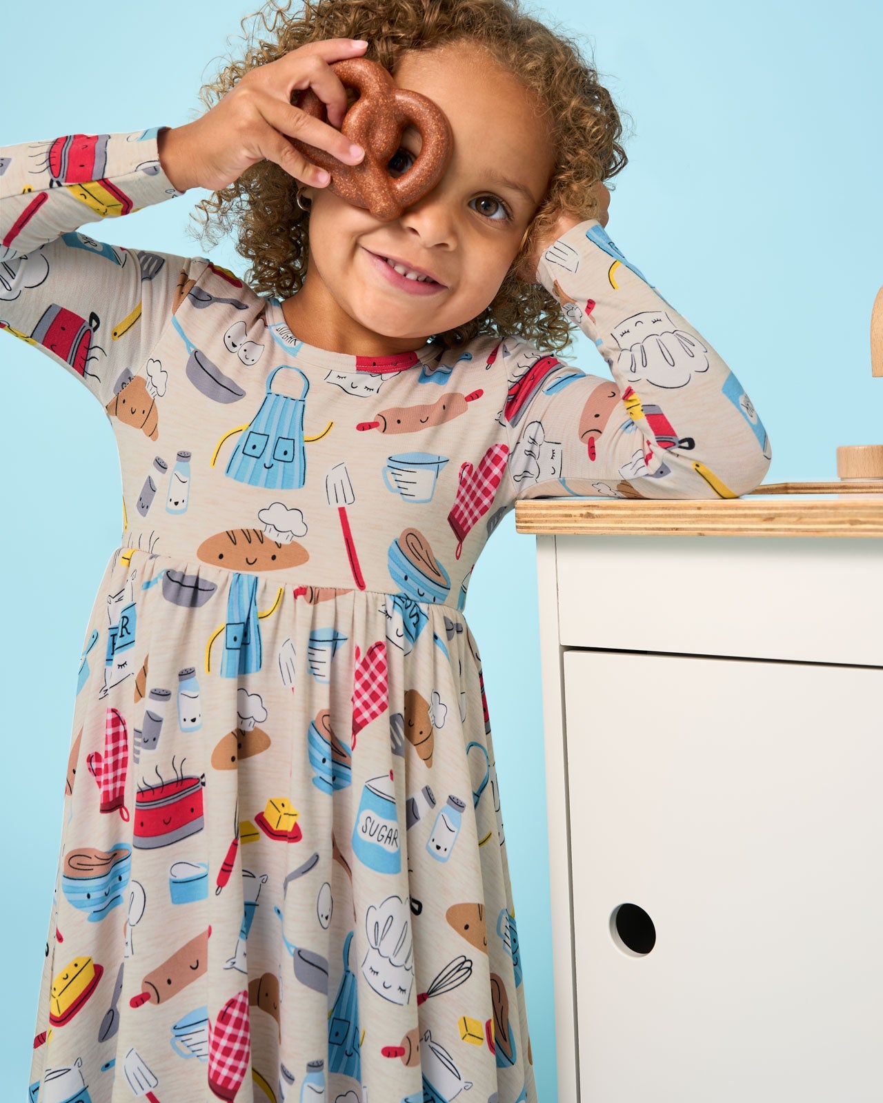 Girl wearing the Little Chef Twirl Dress hold a toy pretzel