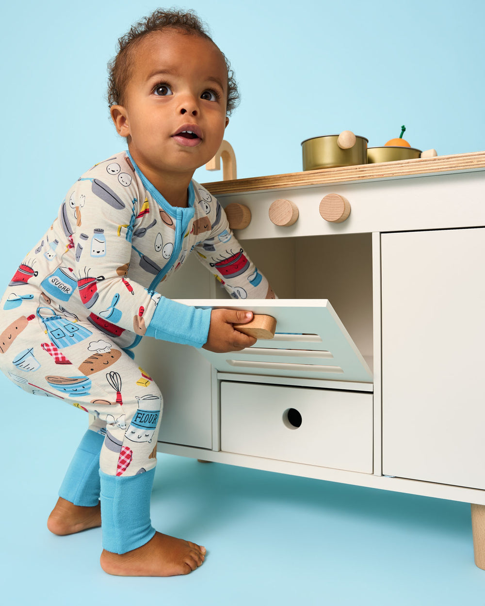 Child wearing the Little Chef Zippy playing with a wooden kitchen