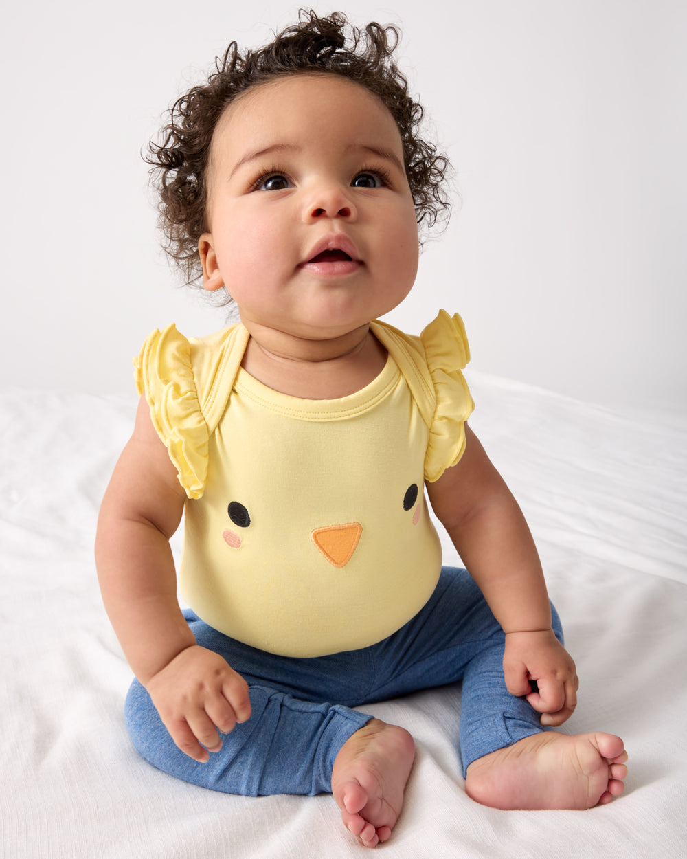 Sitting child wearing the Little Chickie Flutter Bodysuit with blue leggings