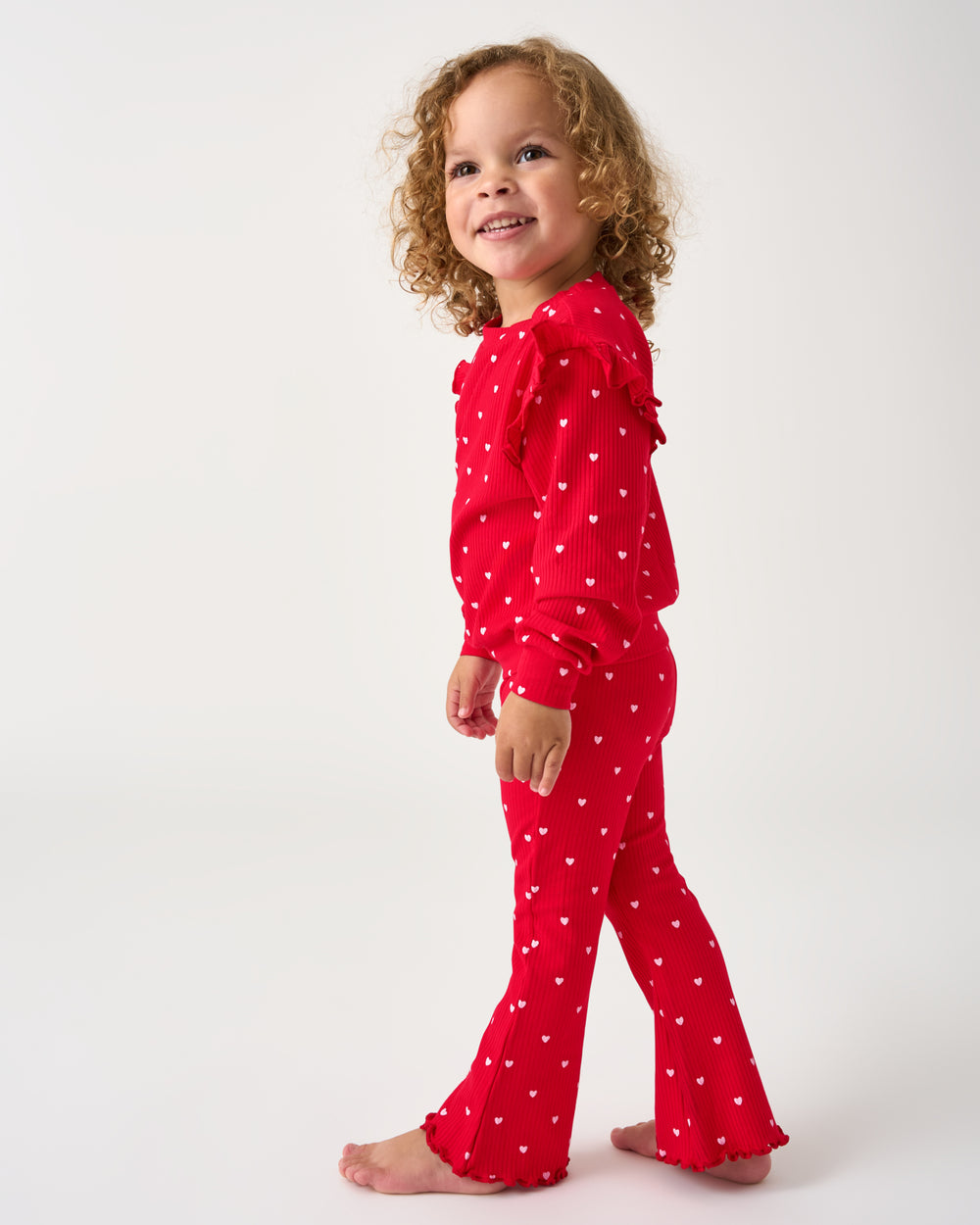 Girl wearing the Little Love Ribbed Flutter Crewneck and flare pants on a white background