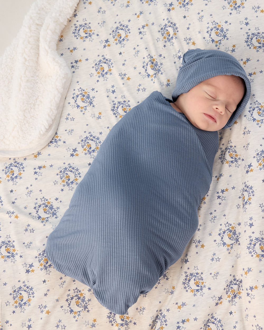 Aerial view of baby in a blue swaddle laying on the Lullaby Sky Mini Cloud Blanket®
