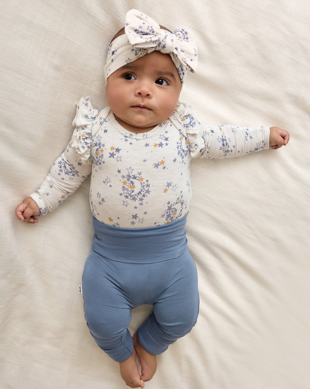 Baby wearing the Lullaby Sky Luxe Bow Headband with a matching girls bodysuit and blue baby leggings