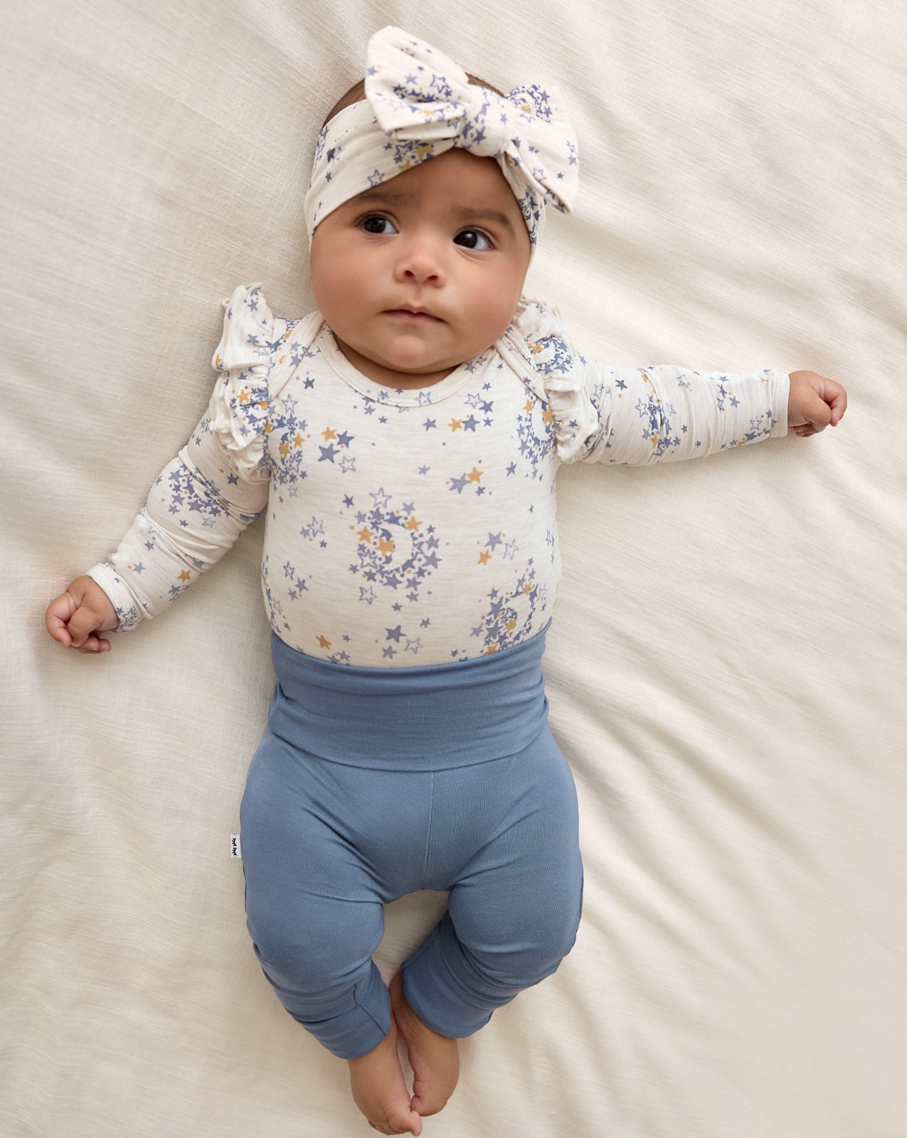 Baby wearing the Lullaby Sky Luxe Bow Headband with a matching girls bodysuit and blue baby leggings