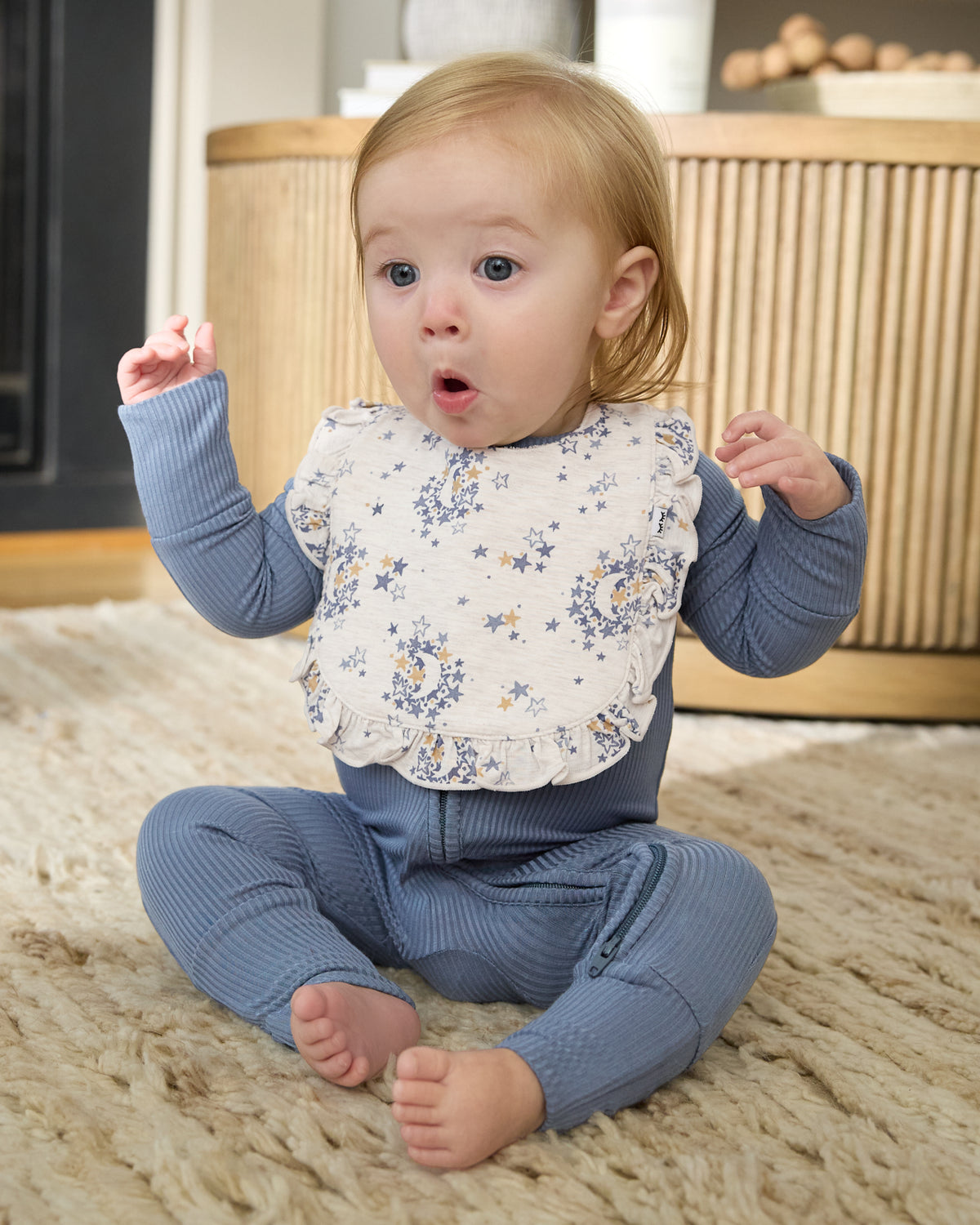Sitting baby wearing the Lullaby Sky Ruffle Bib with blue ribbed pajamas