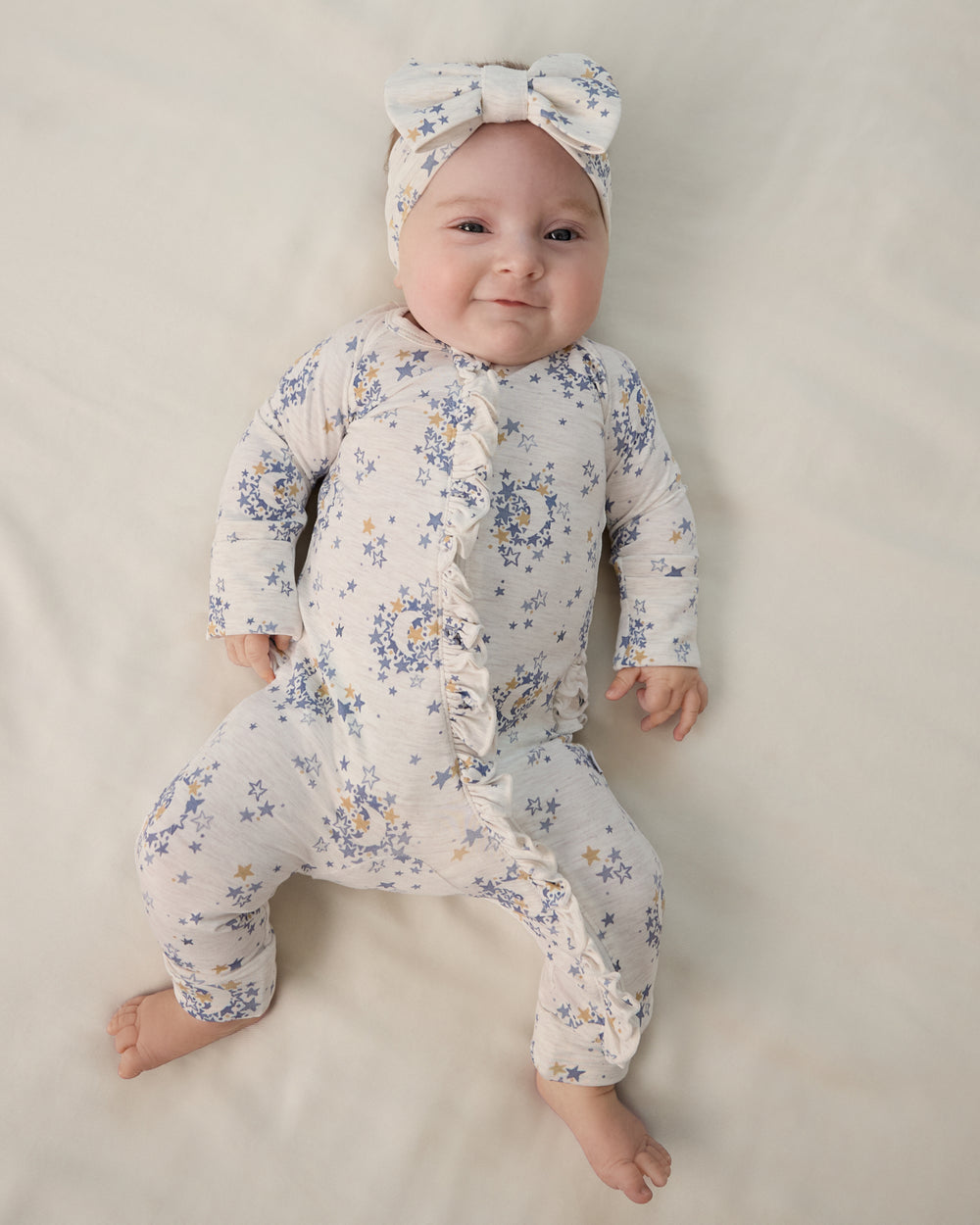Aerial view of newborn wearing the Lullaby Sky Ruffle Zippy and Luxe Bow
