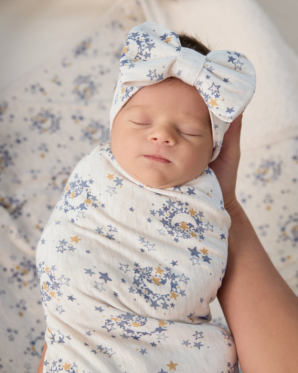 Close up of adult wrapped in the Lullaby Sky Swaddle & Luxe Bow Headband Set