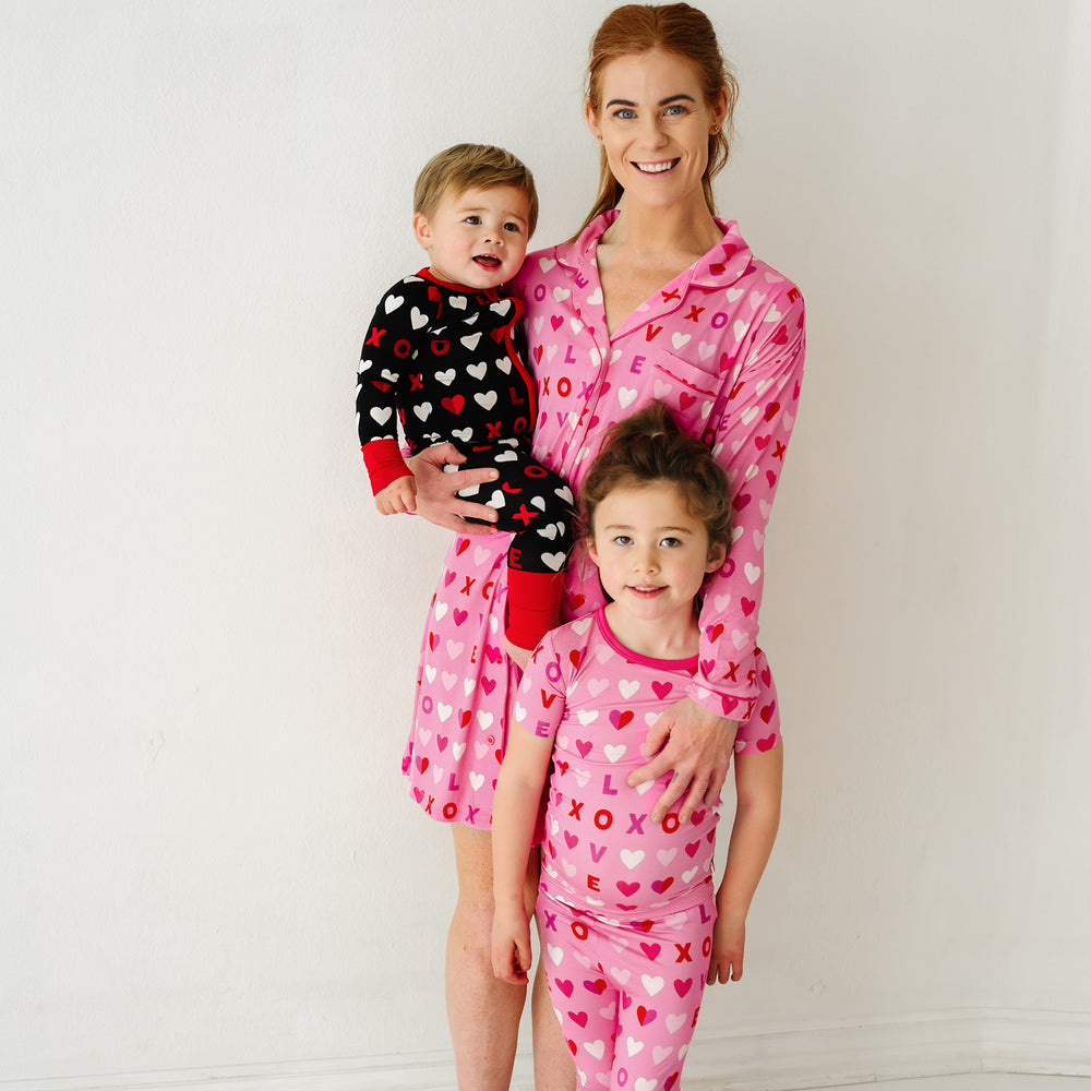 Click to see full screen - Mom posing with her two children. Mom is wearing Pink XOXO women's long sleeve sleep shirt. Kids are wearing Black and Pink XOXO pajamas in two piece and zippy styles.