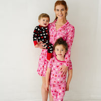 Mom posing with her two children. Mom is wearing Pink XOXO women's long sleeve sleep shirt. Kids are wearing Black and Pink XOXO pajamas in two piece and zippy styles.