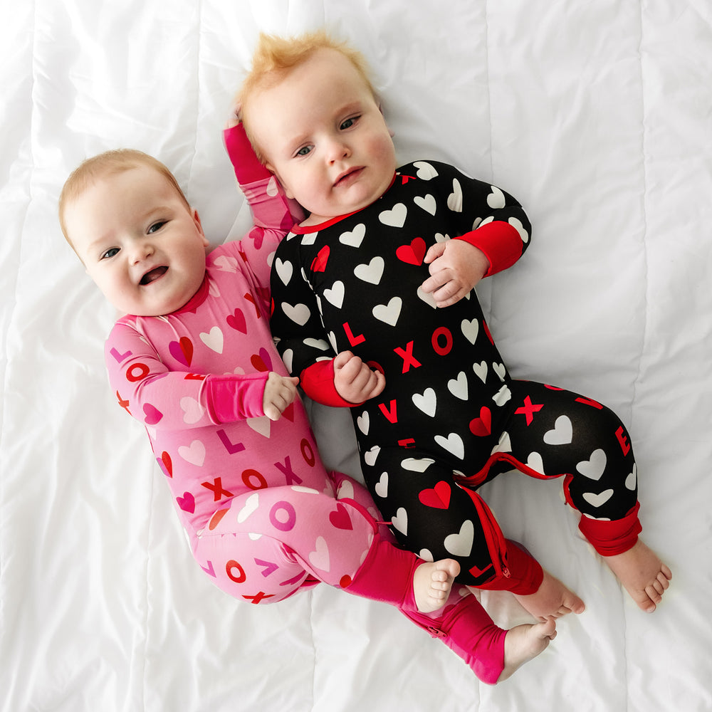 Click to see full screen - Two children laying on a bed wearing matching Black and Pink XOXO crescent zippies
