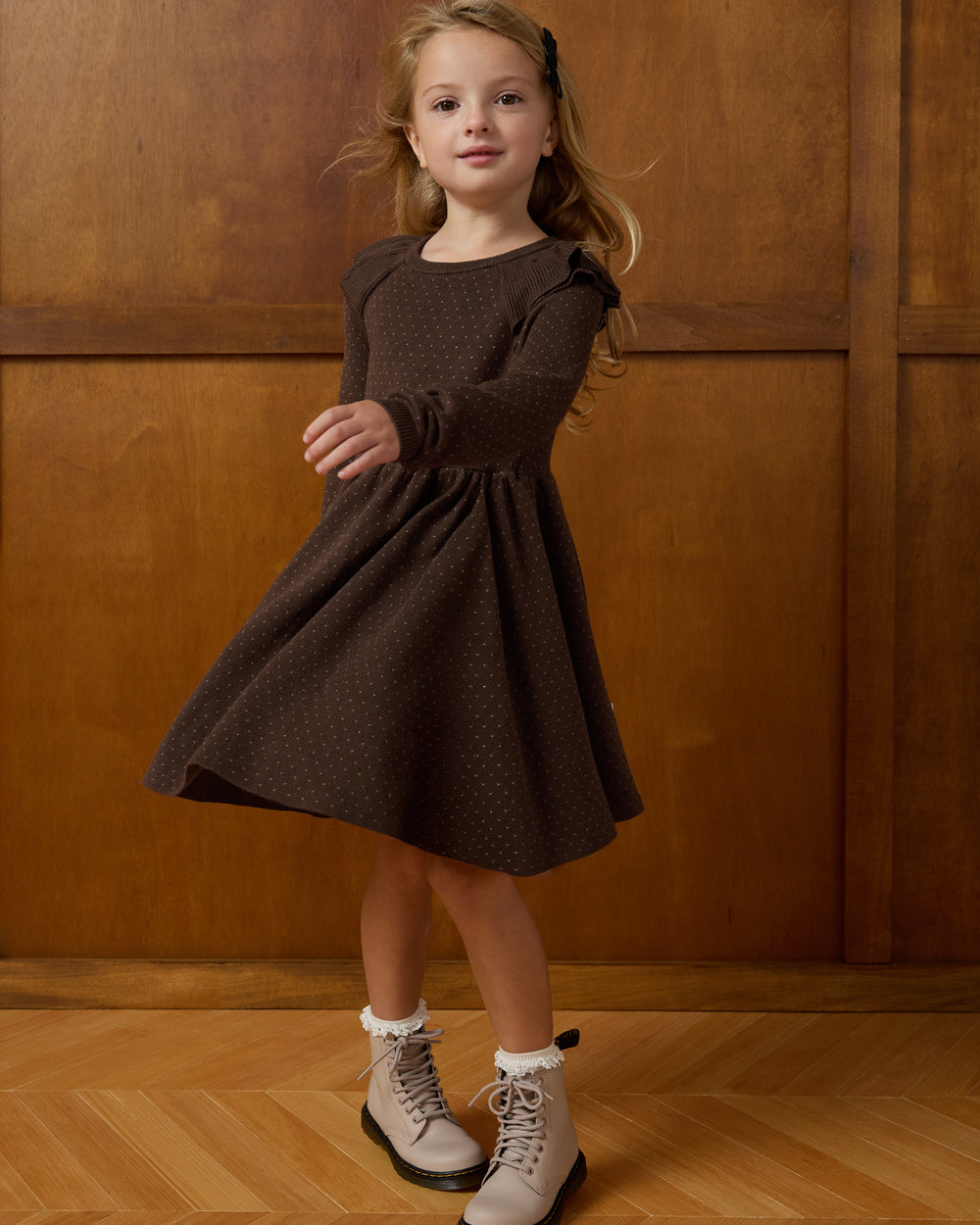 Twirling girl wearing the Mocha Ruffle Sweater Dress on a wooden background