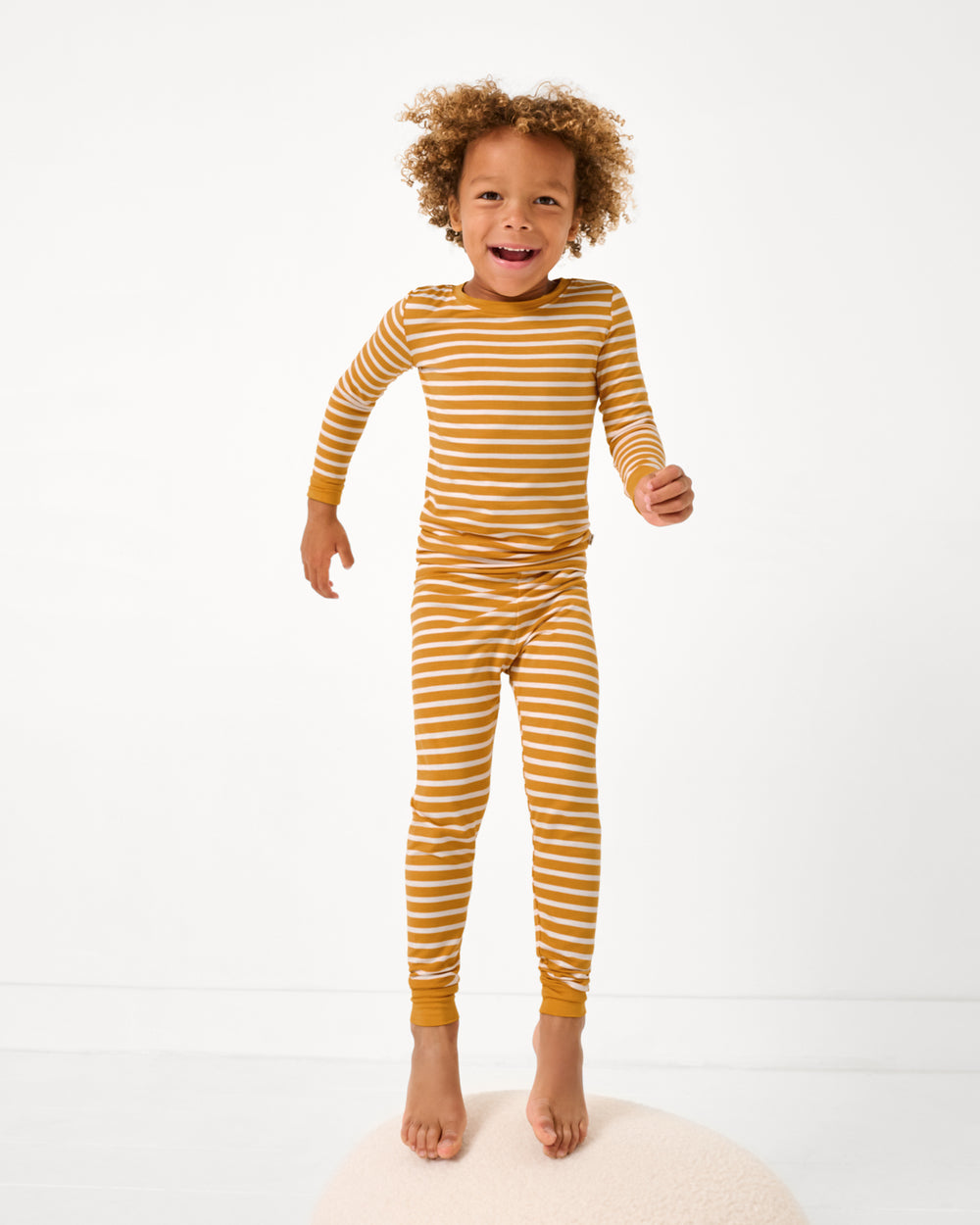 Jumping boy wearing the Marigold Stripe Two-Piece Pajama Set