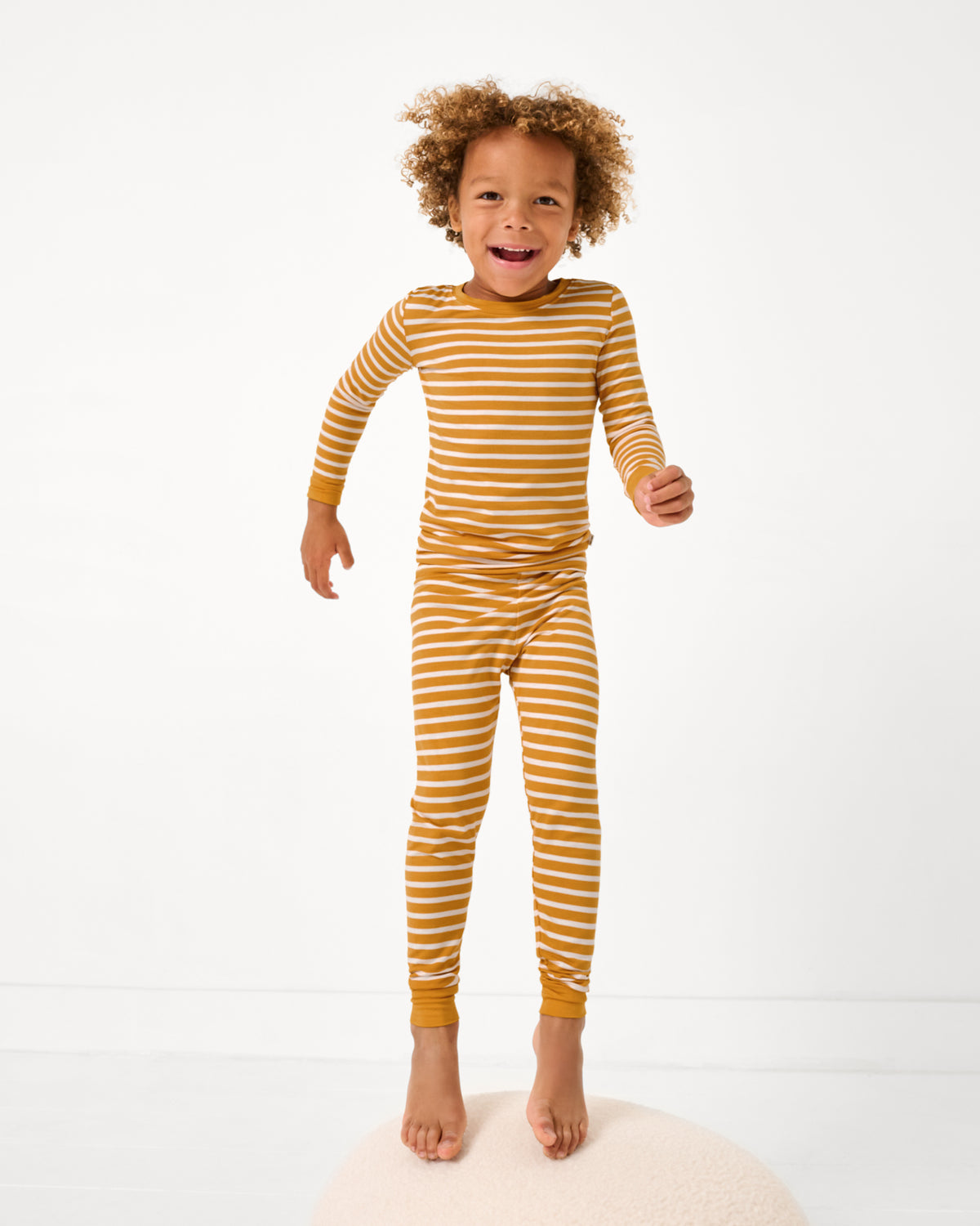 Jumping boy wearing the Marigold Stripe Two-Piece Pajama Set