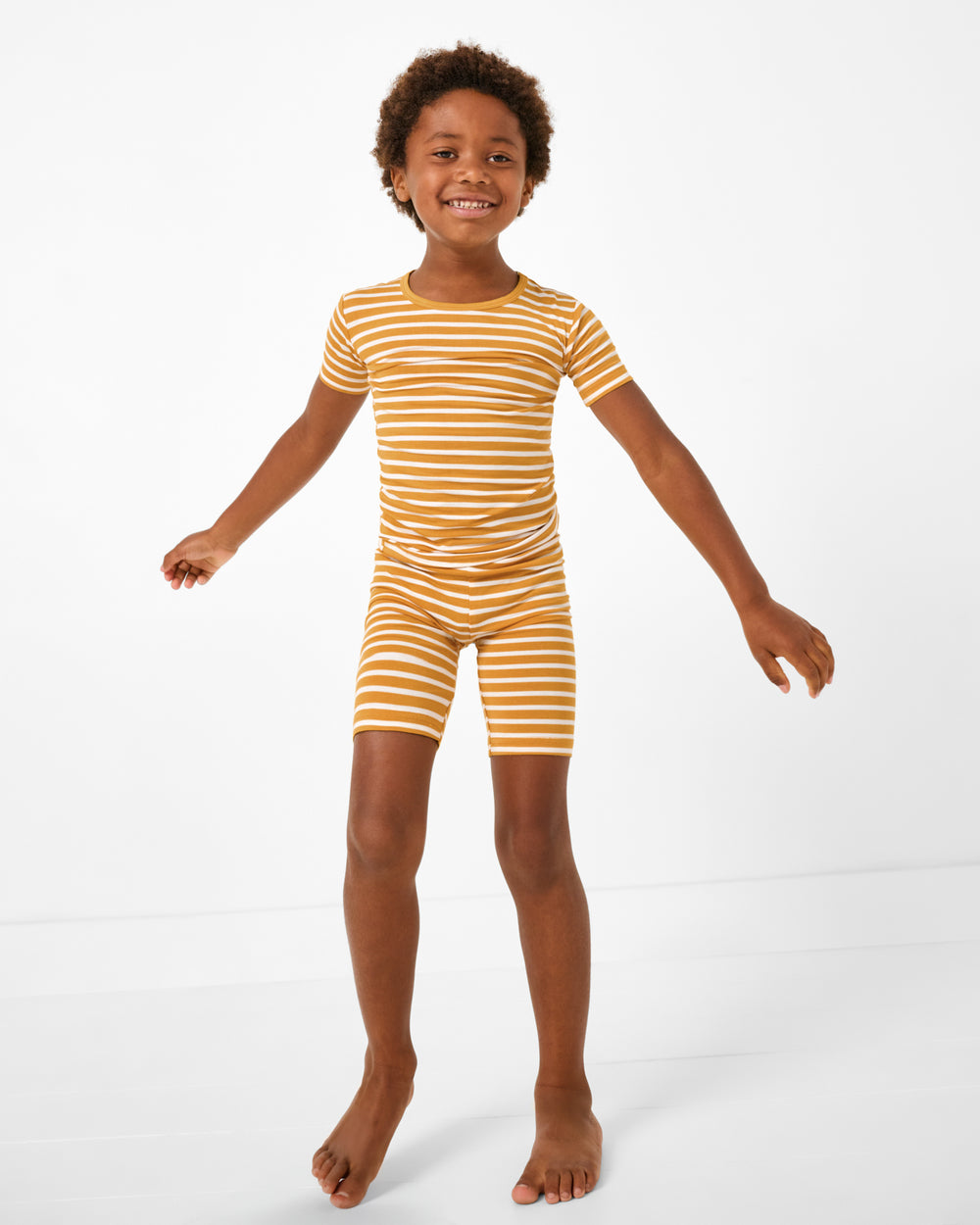 Standing boy wearing the Marigold Stripe Two-Piece Short Sleeve & Shorts Pajama Set