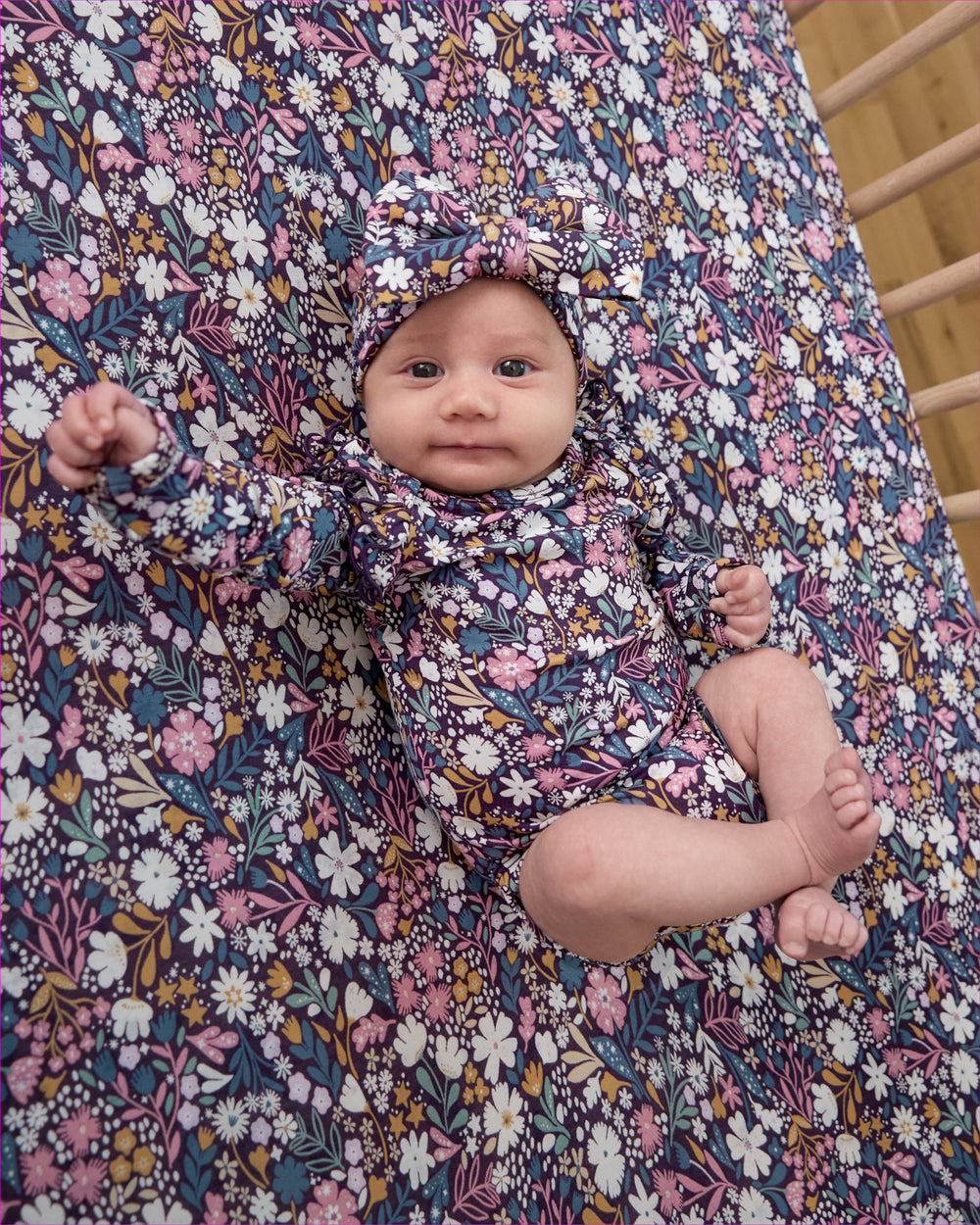Newborn wearing the Midnight Petals Flutter Bodysuit on a matching crib sheet