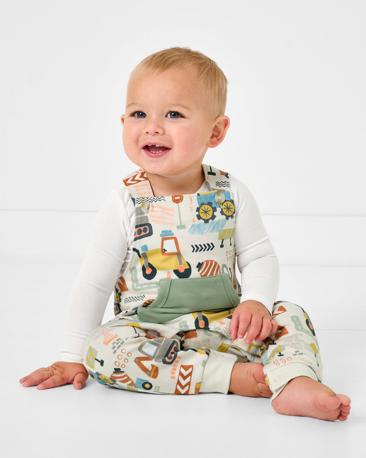 Sitting child wearing the Mini Builders Overall Romper