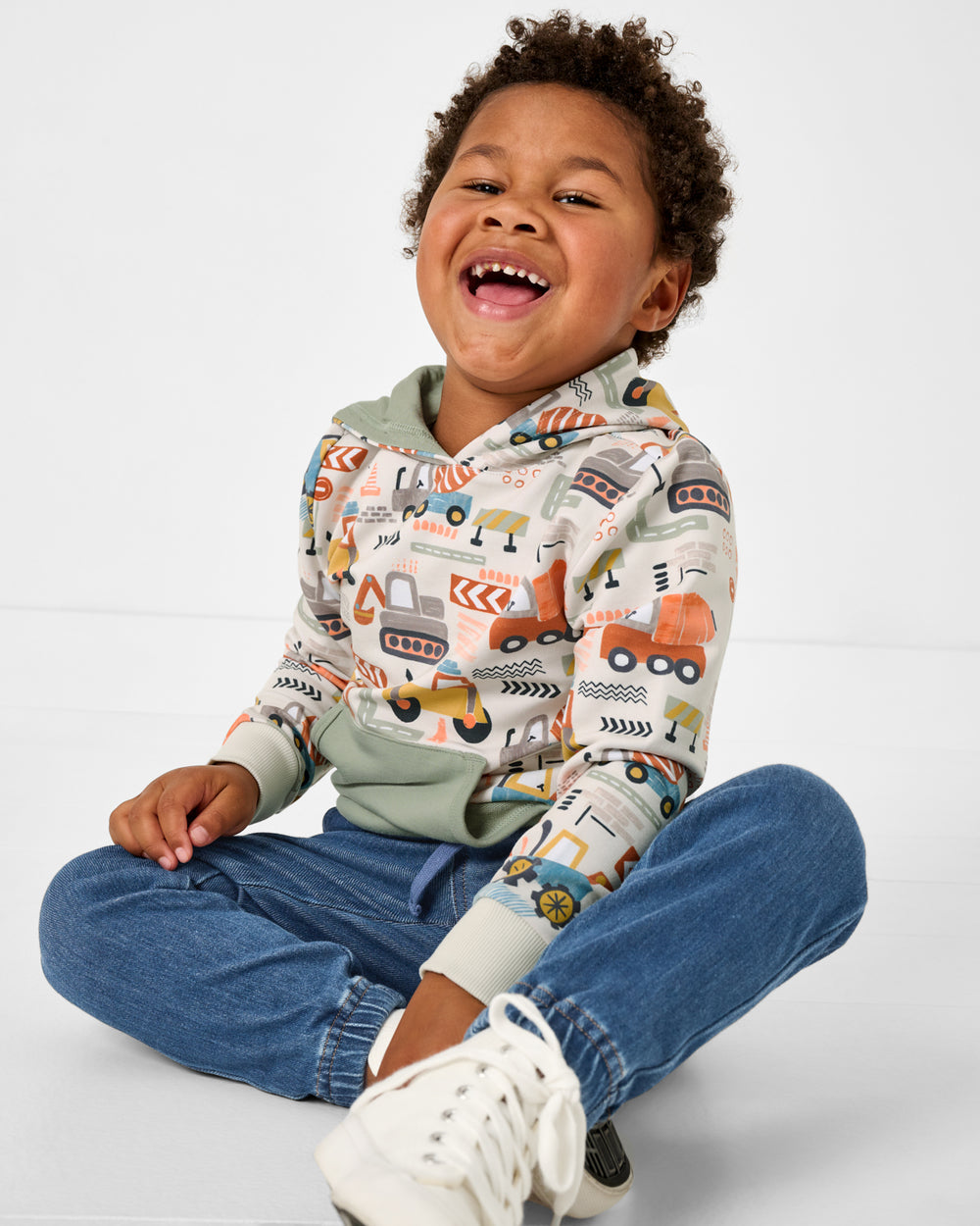 Sitting boy wearing the Mini Builders Pullover Hoodie with denim joggers