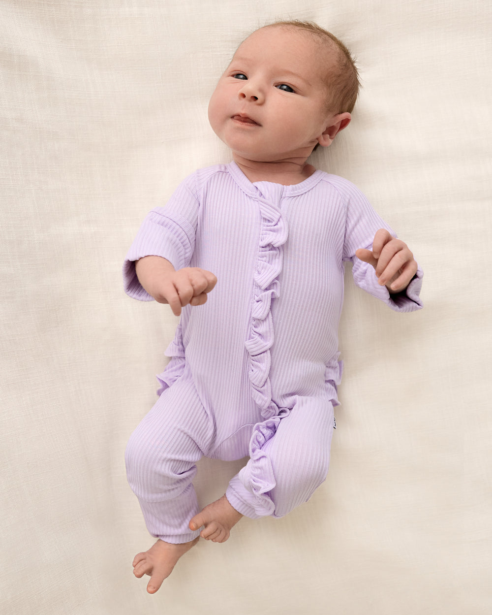 Aerial view of baby wearing the Misty Lavender Ribbed Ruffle Zippy