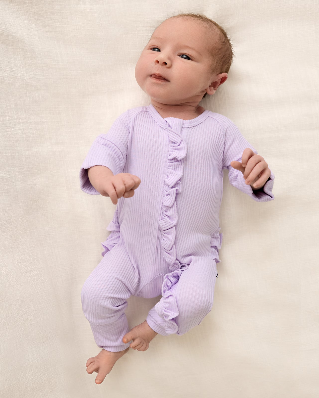 Aerial view of baby wearing the Misty Lavender Ribbed Ruffle Zippy
