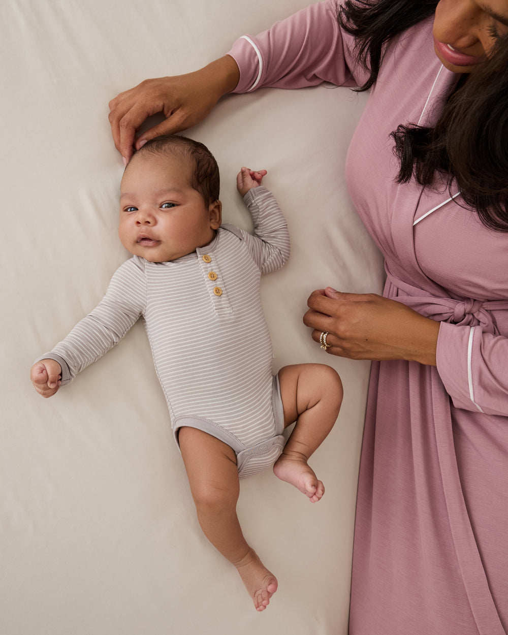 Mother and newborn on a bed wearing styles from the Newborn Capsule