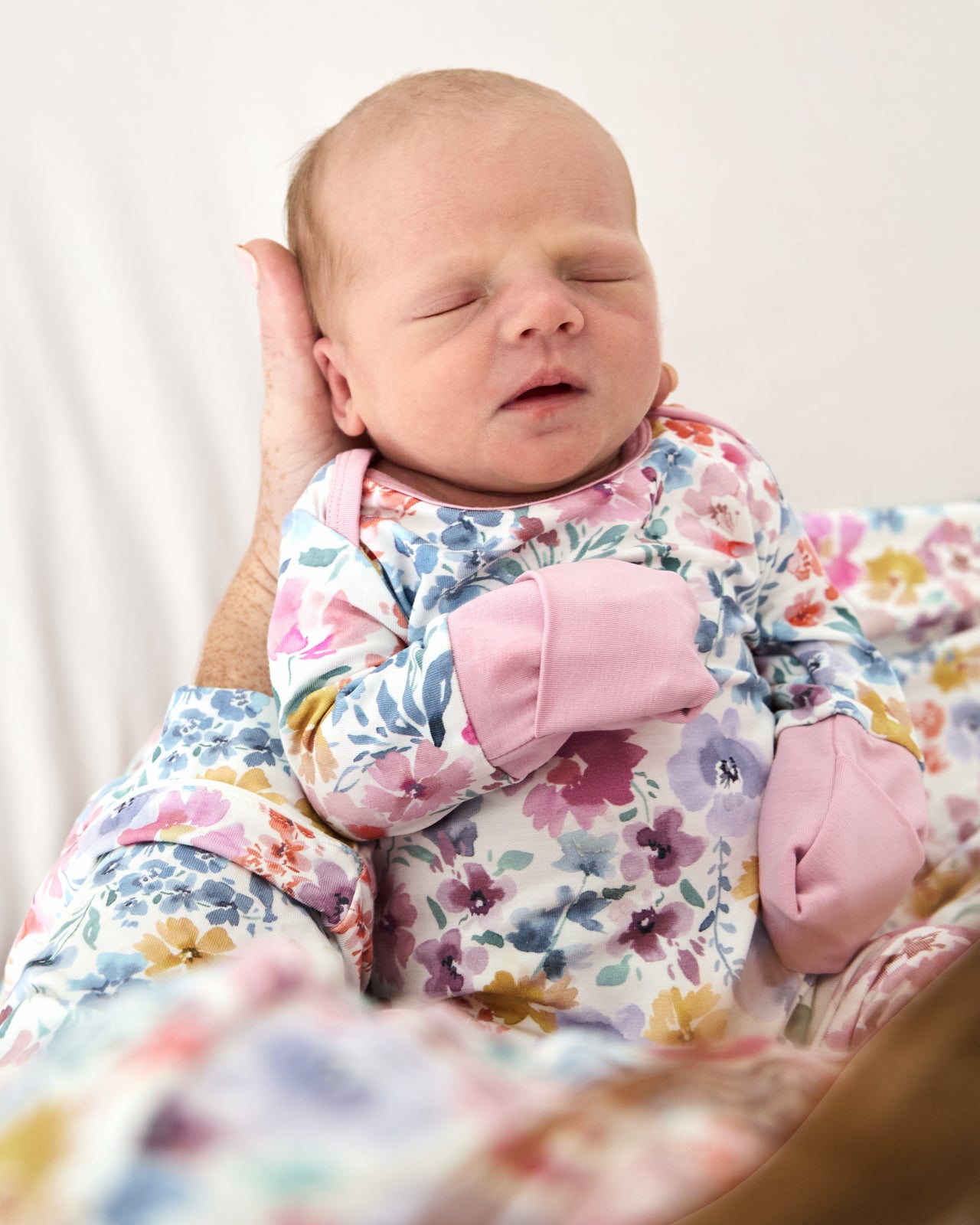 Newborn wearing the Tiny Blooms Crescent Zippy being held