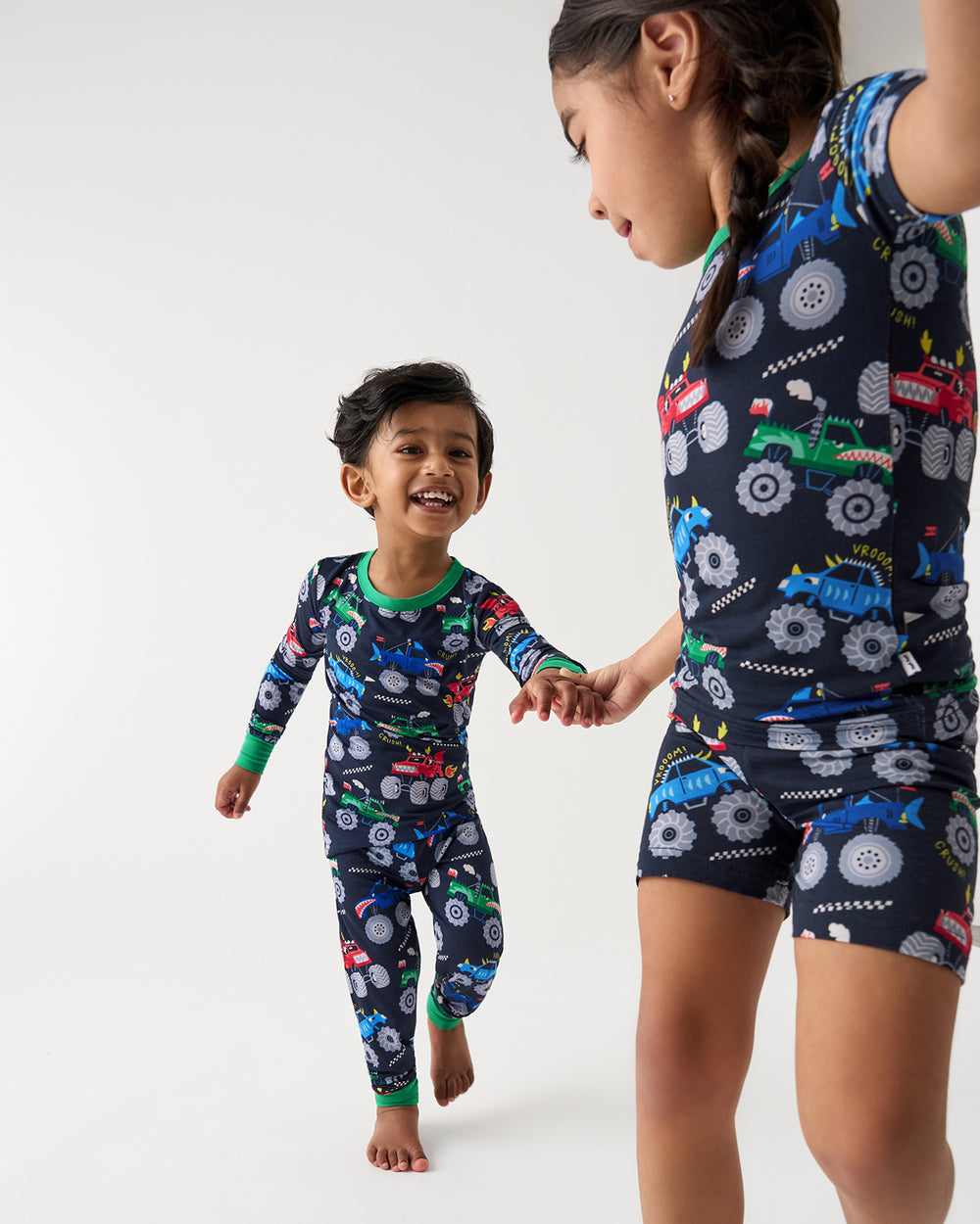 Two children wearing matching Monster Truck Madness Two-Piece Pajama Sets