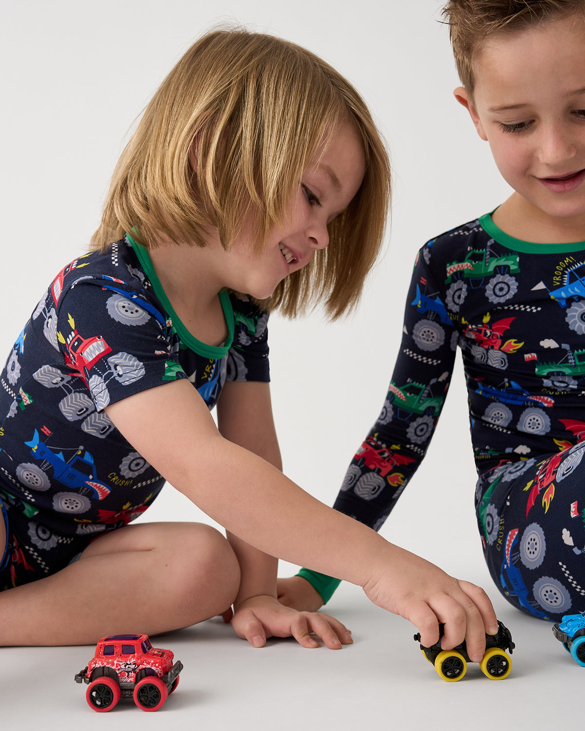 Two kids playing with truck toys wearing matching Monster Truck Madness Two-Piece Pajama Sets