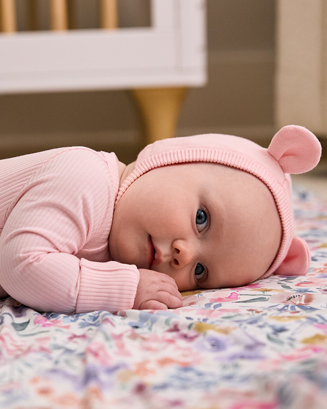 Newborn laying on a floral blanket wearing the Prima Pink Bear Bonnet