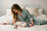 Woman in pajamas sitting on a bed with a baby wearing a Sweet Safari Zippy.